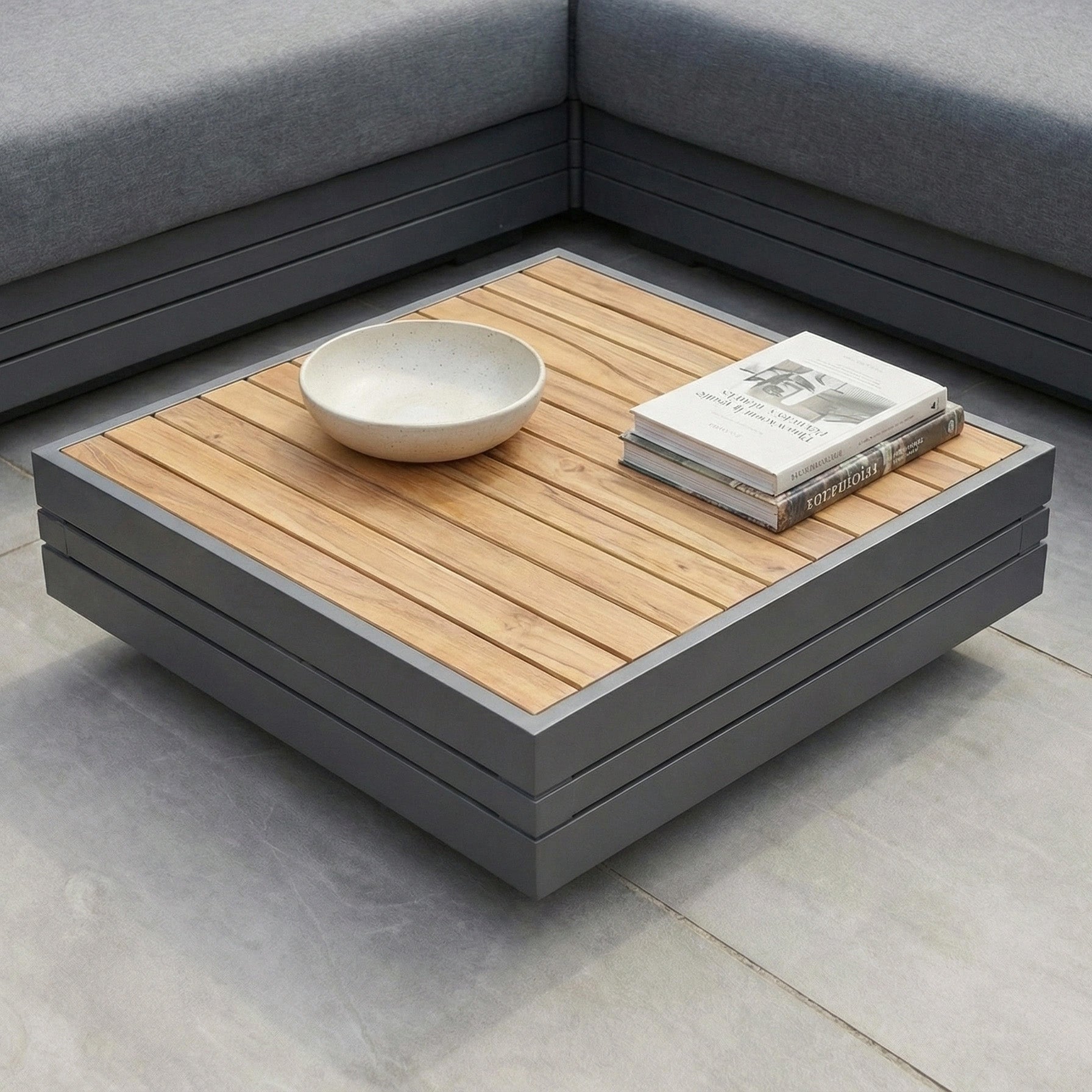 The Panama Teak Coffee Table, styled with a ceramic bowl and magazines, is surrounded by gray cushioned seating—an inviting luxury outdoor piece ideal for gatherings.