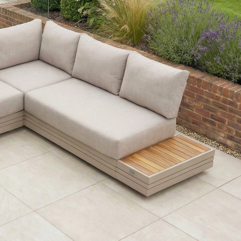 Modern outdoor sectional sofa with light cushions on a tiled patio, paired with the elegant Panama Teak Side Table in Latte, surrounded by plants and a low brick wall. Durable aluminium frame ensures lasting beauty for your outdoor setup.