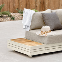 Outdoor patio sofa with beige cushions on a contemporary aluminum frame, a gray throw draped over the arm, and a straw hat with polka dot ribbon on it, complemented perfectly by the Panama Teak Side Table in Latte.
