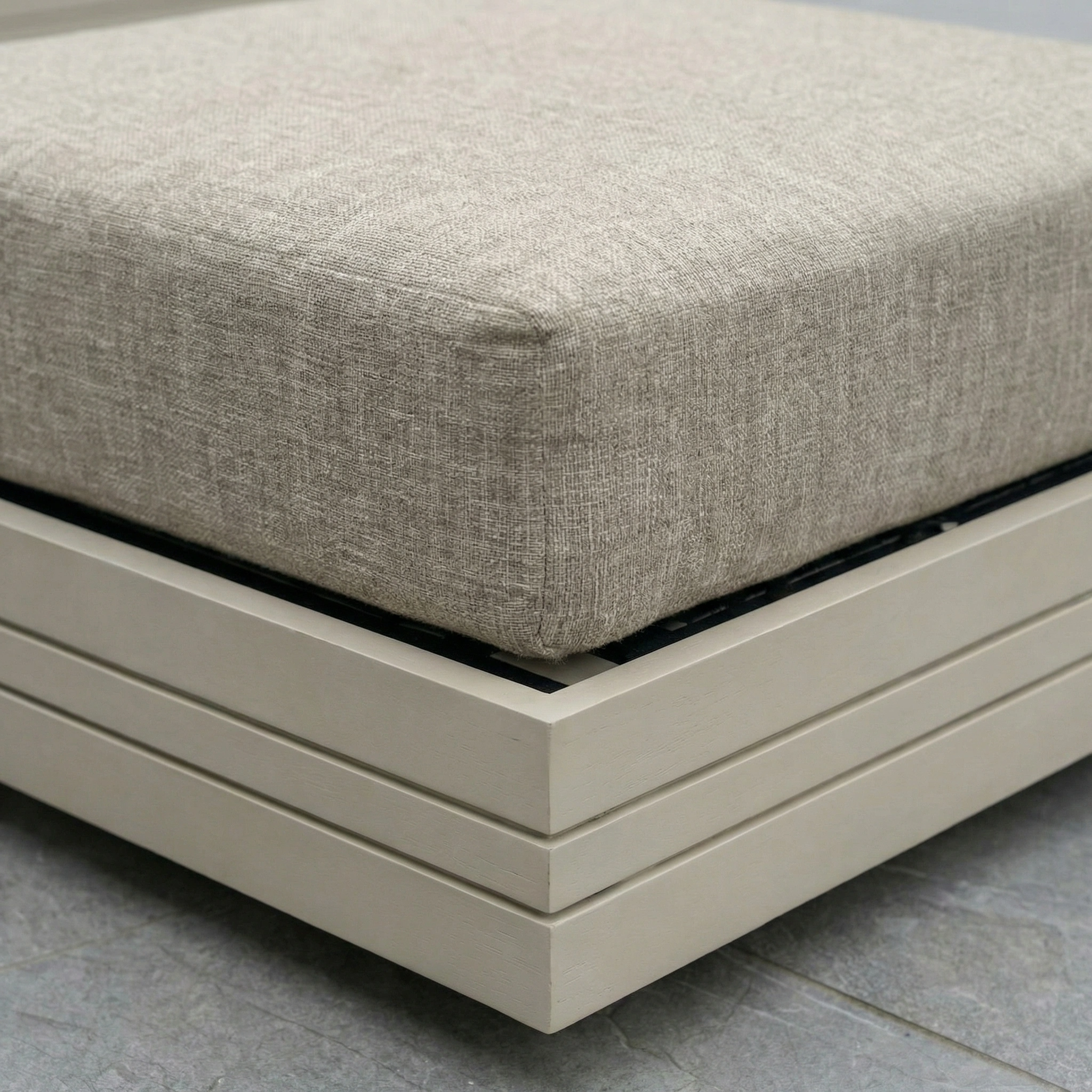 Close-up of the Panama Corner Unit/Footstool in Latte, featuring a beige cushion on a light wooden frame, as part of a modular sofa set on a gray stone floor.