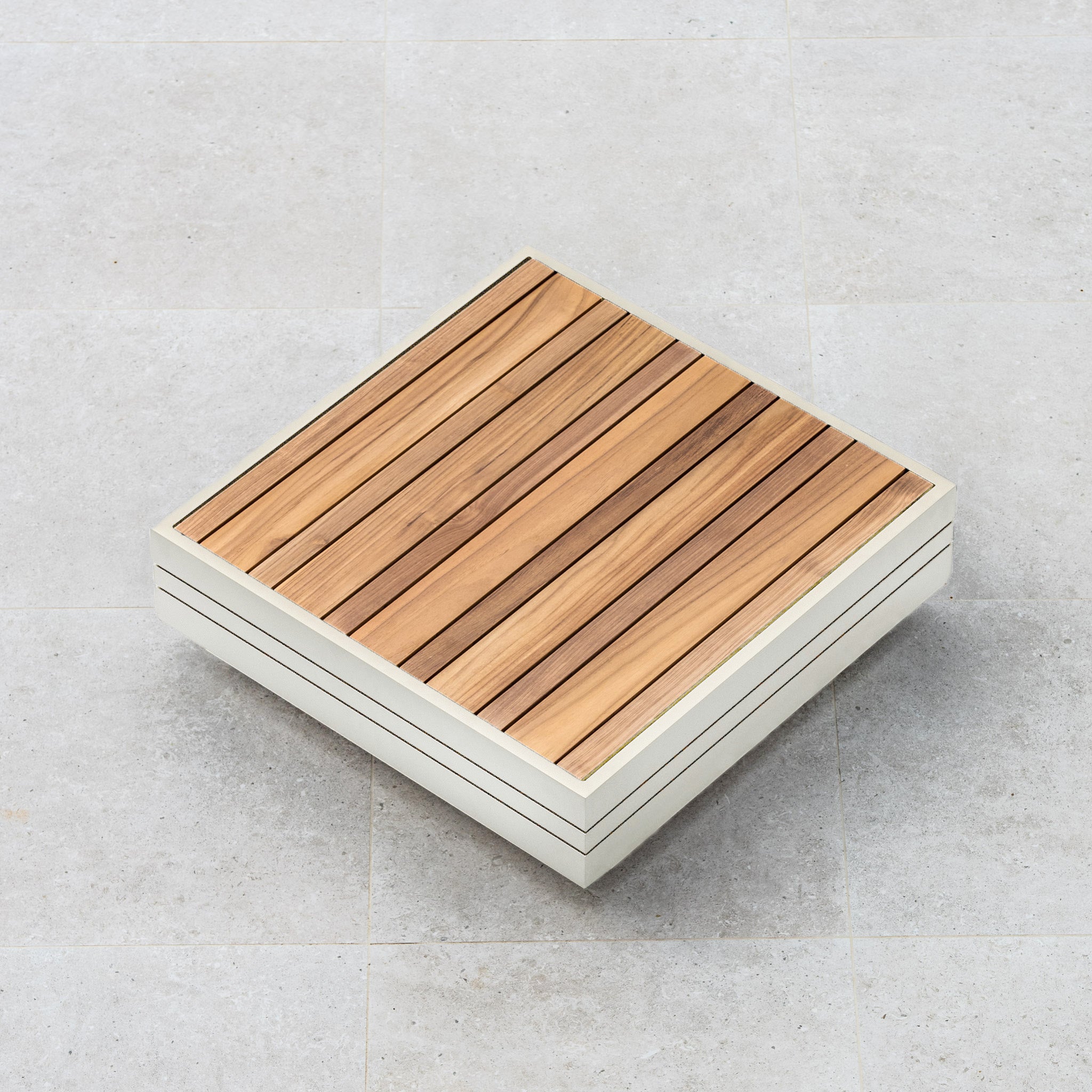 A square wooden tabletop with a light frame sits on a light gray tiled floor, echoing the design of the Panama Luxury Outdoor L-Shape Corner Group Set in Latte from Harbour Lifestyle, which is crafted from sustainable teak.