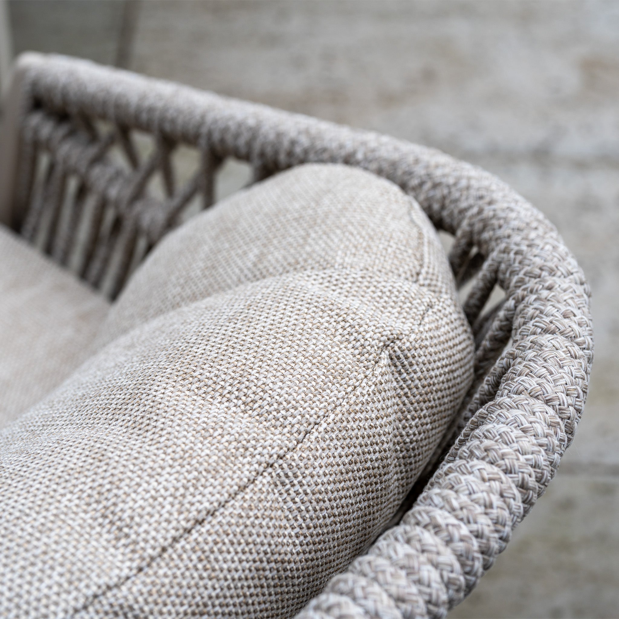 Close-up of a beige woven outdoor chair from the Pello 4 Seat Round Dining Set with Albatross Table in Fawn, featuring a textured cushion and braided armrest—ideal for elevating your outdoor dining furniture.