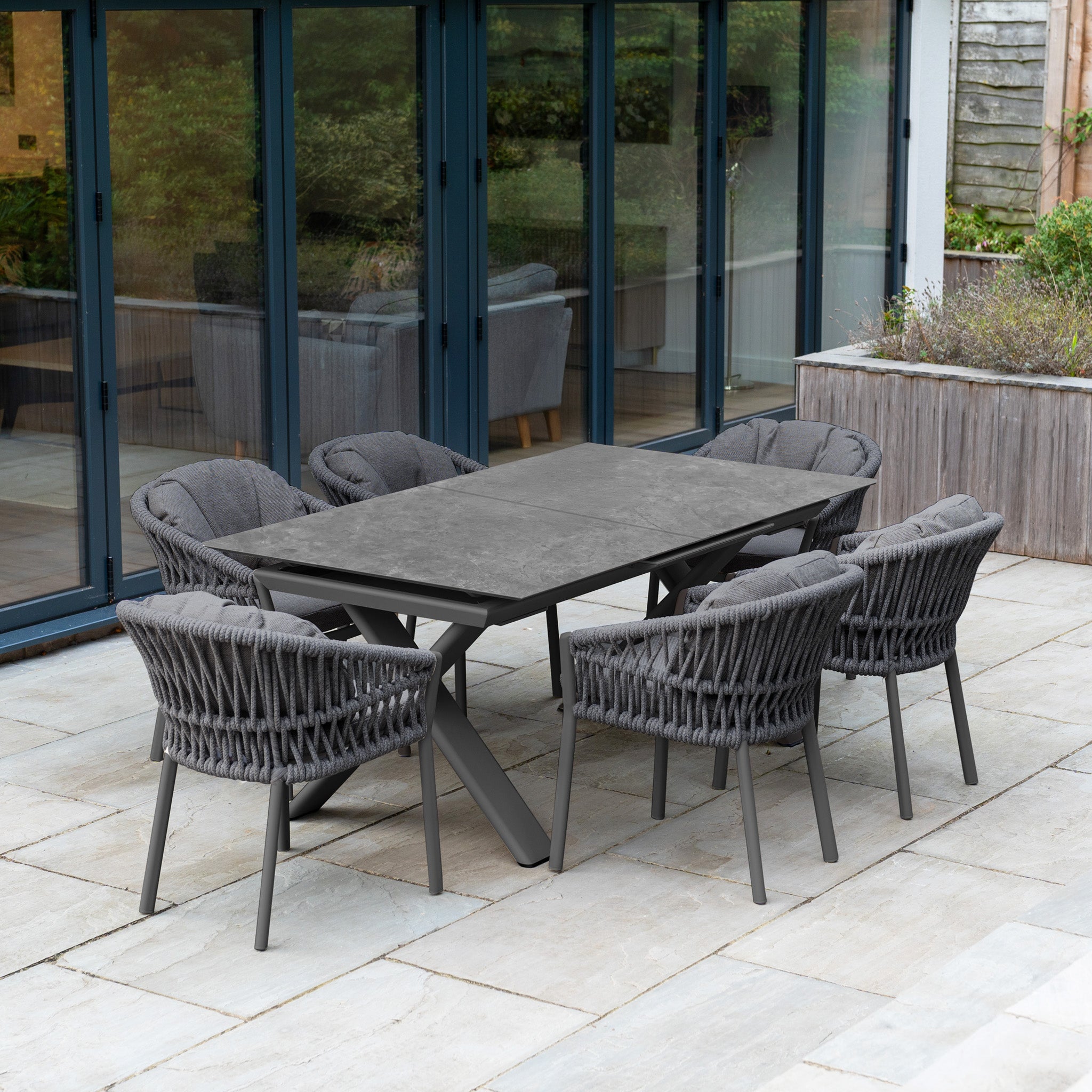 The Pello 6 Seat Dining Set with Albatross Extending Table in Grey offers stylish outdoor dining for gatherings on your stone patio by the glass doors. Includes six cushioned chairs and a versatile, extendable table.