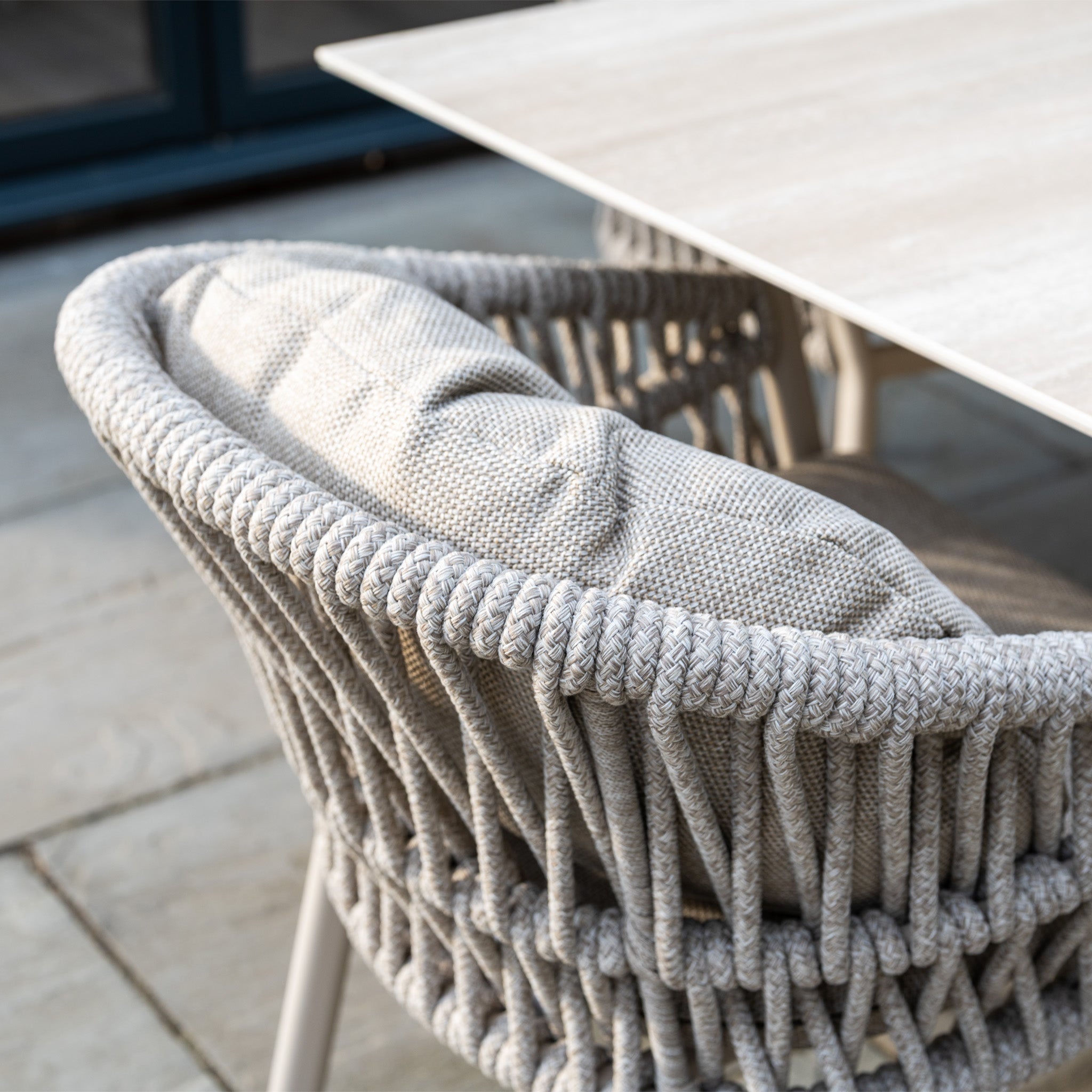 Close-up of a gray woven outdoor dining chair with a light gray cushion, from the stylish Pello 6 Seat Dining Set with Albatross Extending Table in Fawn.