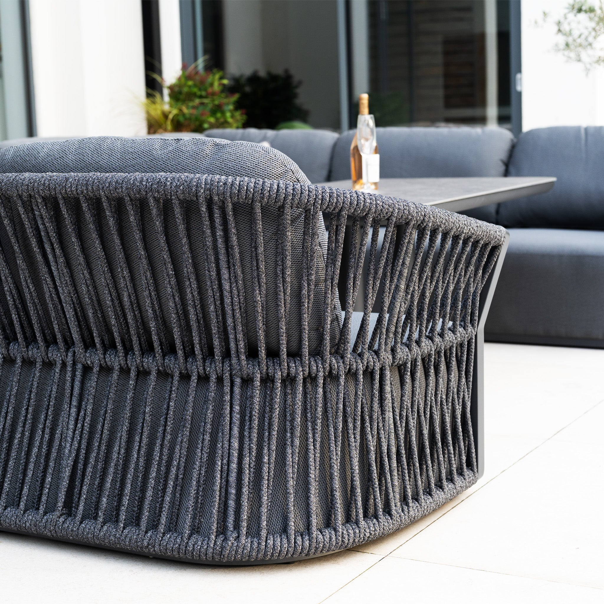 Close-up of the Pello U-Shape Corner Sofa Set with Altura Rising Table in Grey on a patio, featuring modern woven garden furniture and an outdoor dining set in the background.
