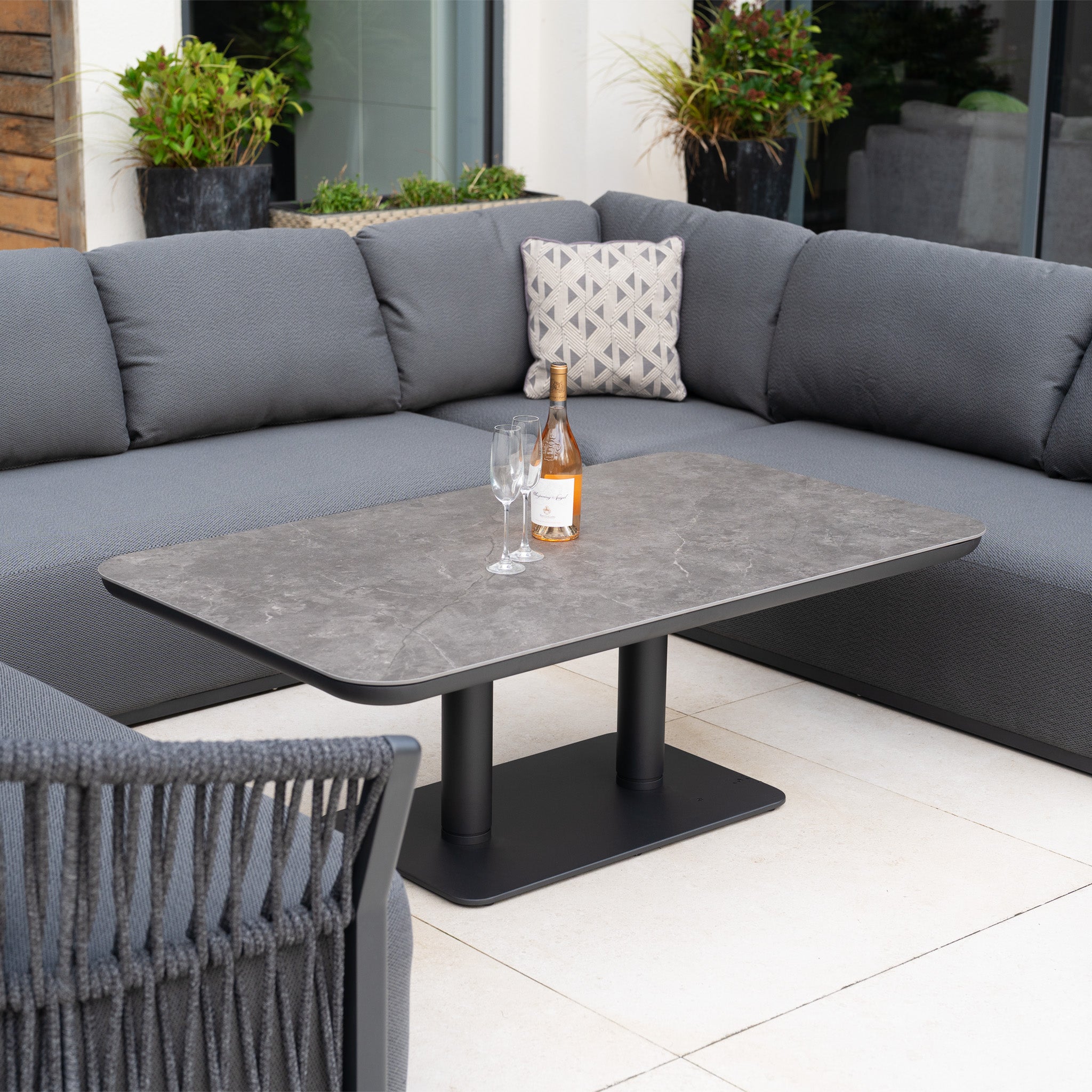 The Pello U-Shape Corner Sofa Set with Altura Rising Table in Grey offers a stylish outdoor setup, featuring a rectangular table perfect for holding drinks and creating a relaxing garden atmosphere.