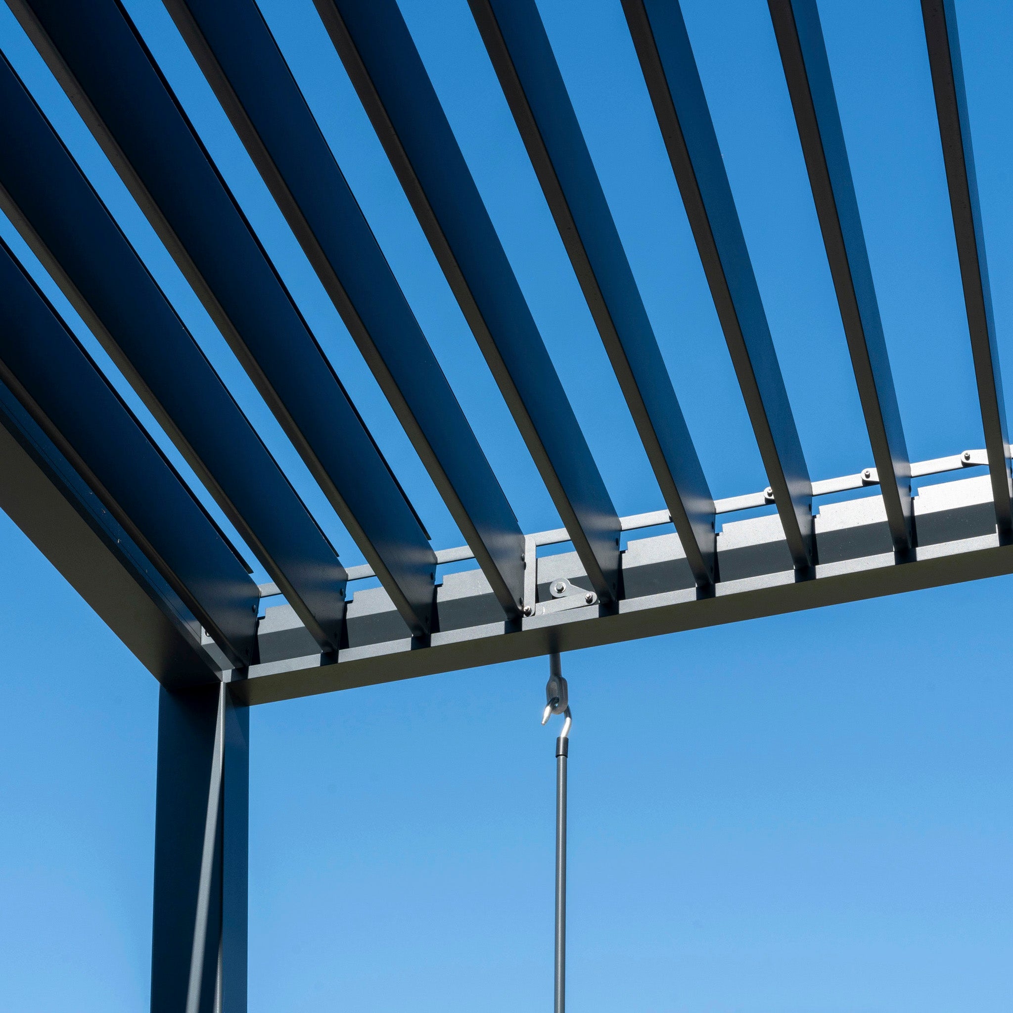 A close-up of the PergoSTET Lite 3m x 3m Metal Square Pergola in Grey showcases its modern roof with sleek metal slats and a built-in drainage system against a clear blue sky.