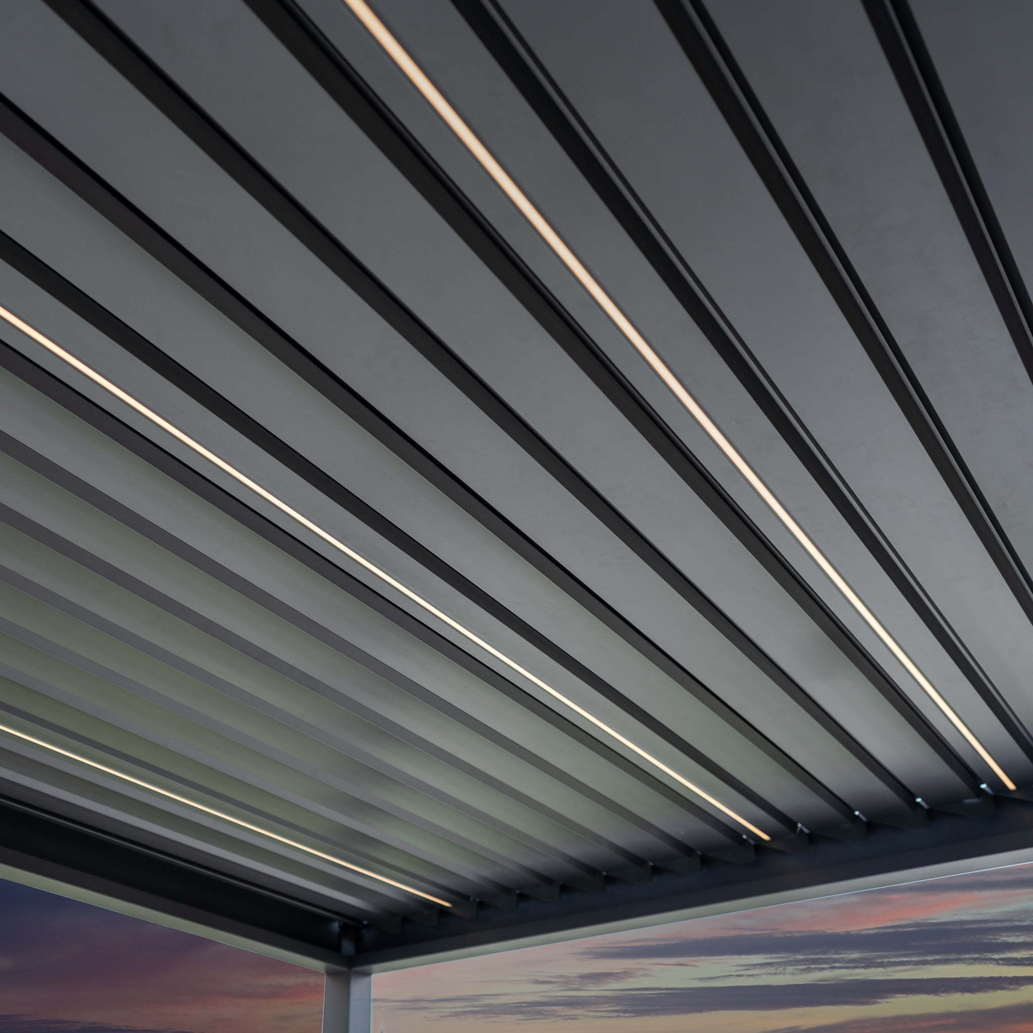 The PergoSTET Deluxe 3m x 6m Rectangular Pergola features motorised LED louvres and a grey finish, perfect against a sunset sky, with remote-controlled functionality.