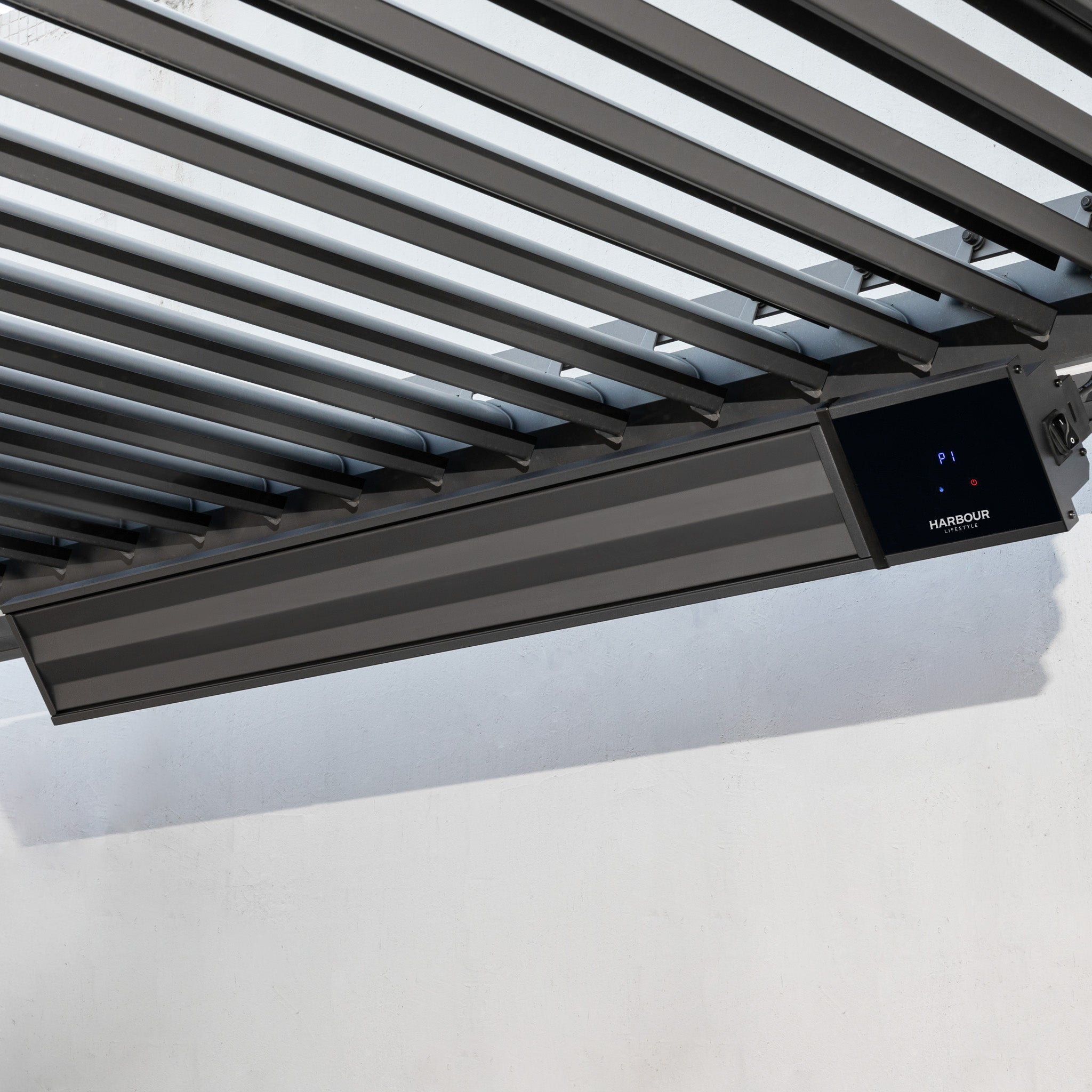 A PergoSTET 2400W Wifi & Bluetooth Heater in Black is mounted under a slatted metal pergola roof against a white wall, delivering efficient outdoor heating.
