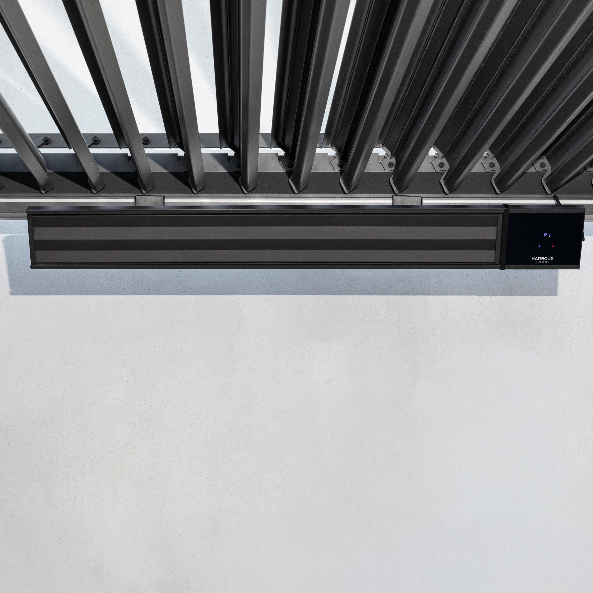 The PergoSTET 2400W Wifi & Bluetooth Heater in Black from Harbour Lifestyle is mounted on a white wall beneath metal slats, providing stylish outdoor heating ideal for pergolas.
