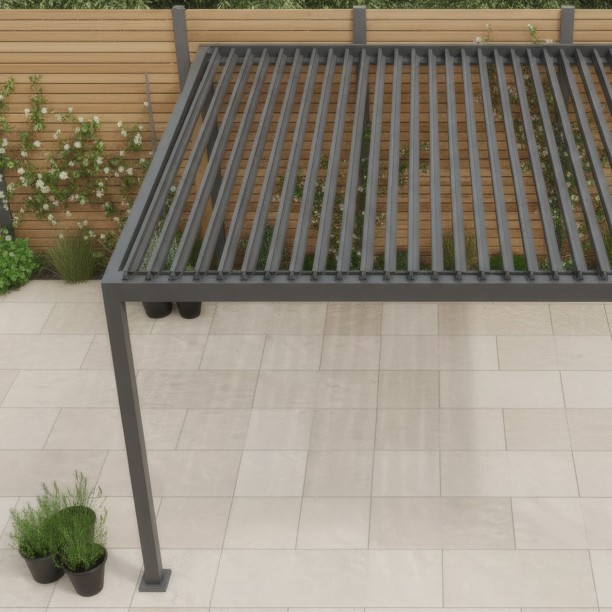 The PergoSTET Lite 2.4m x 3m Metal Rectangular Pergola in Grey features tilting louvres and provides stylish outdoor shade, perfect for a tiled patio surrounded by wooden fencing and potted plants.