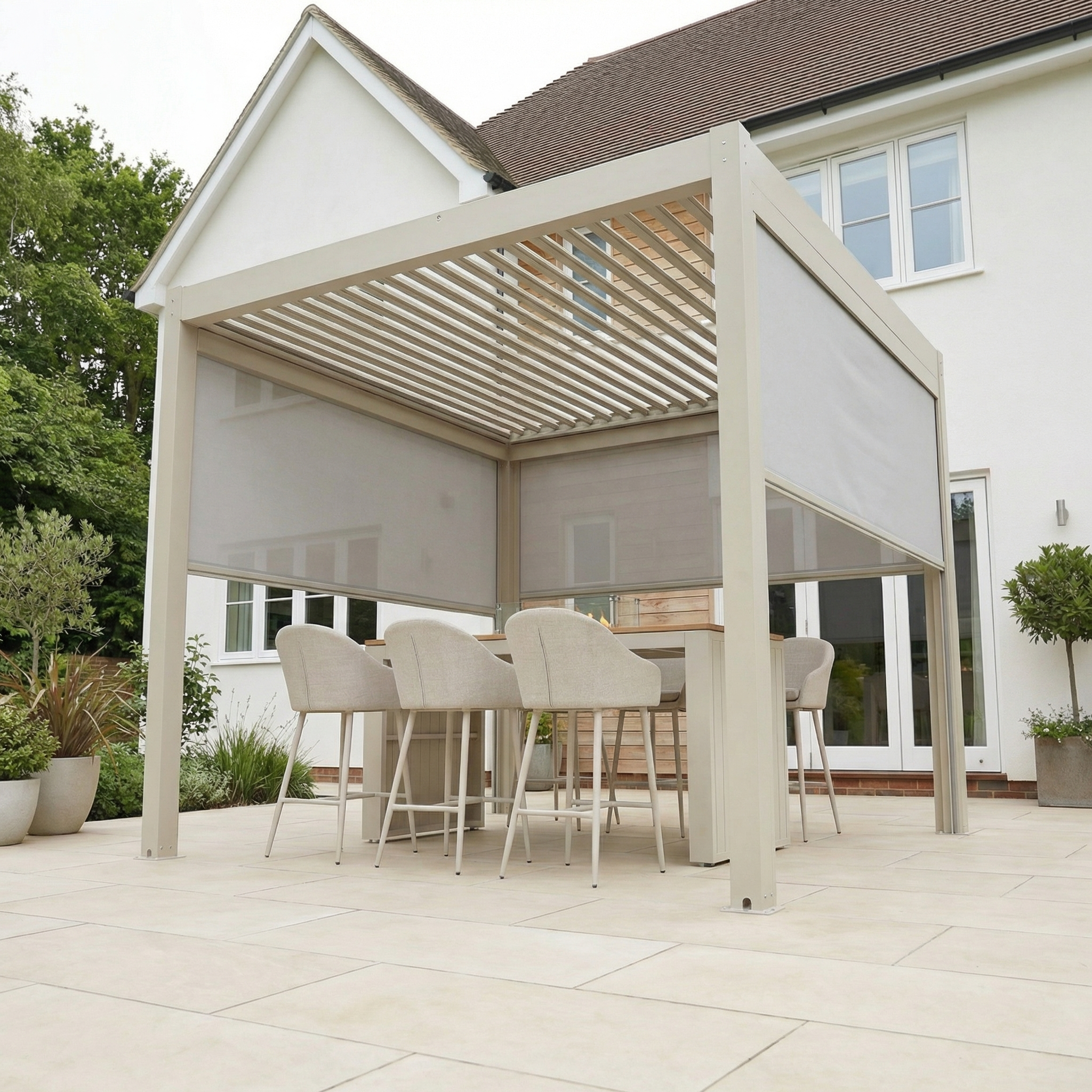Contemporary outdoor dining area with a PergoSTET Plus 3m x 3m Square Pergola in Latte, featuring 3 manual side blinds and LED lighting, six chairs, a table, and tiled patio beside a white house for added comfort.