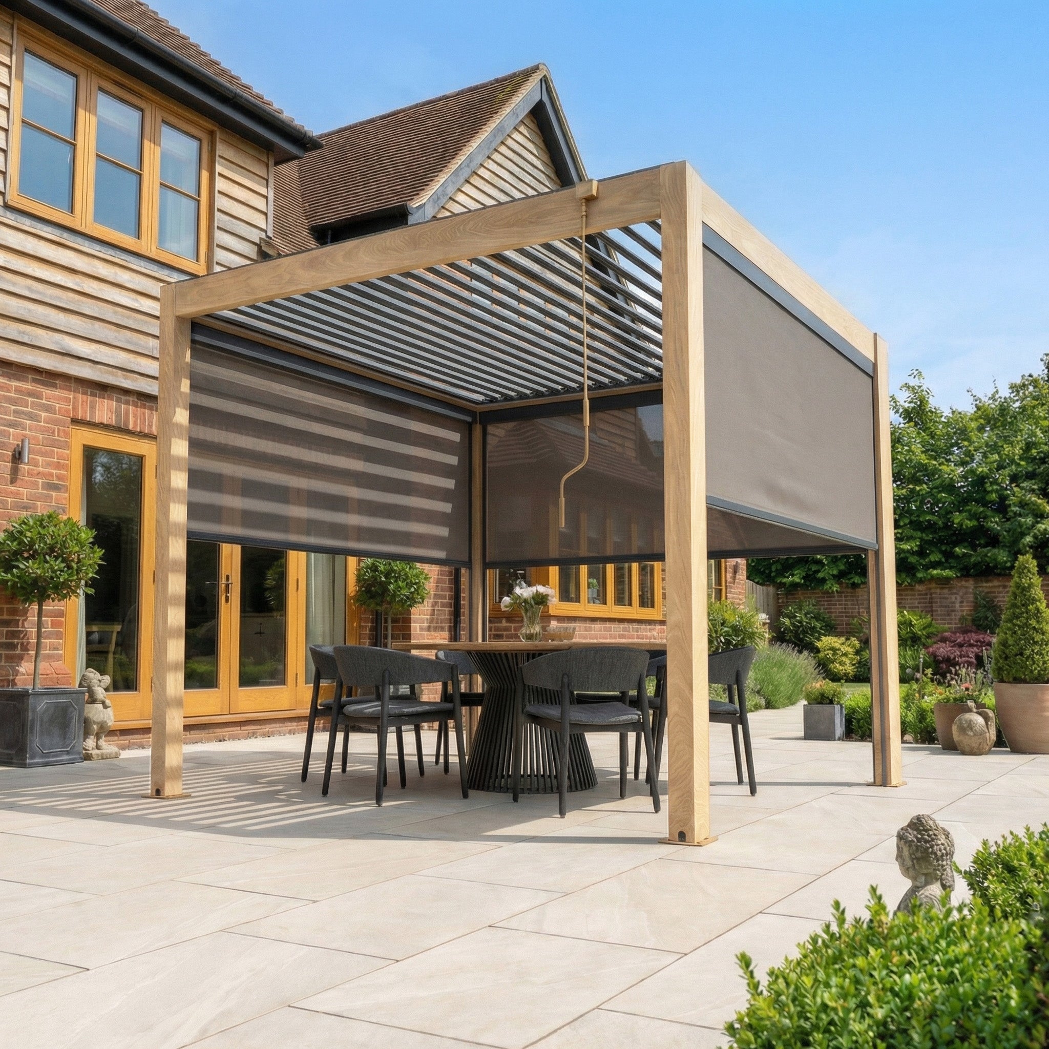Contemporary outdoor dining area featuring a PergoSTET Plus 3m x 3m Square Pergola with wood effect, 3 manual side blinds, LED lighting, and a sleek black table and chairs on a tiled patio.