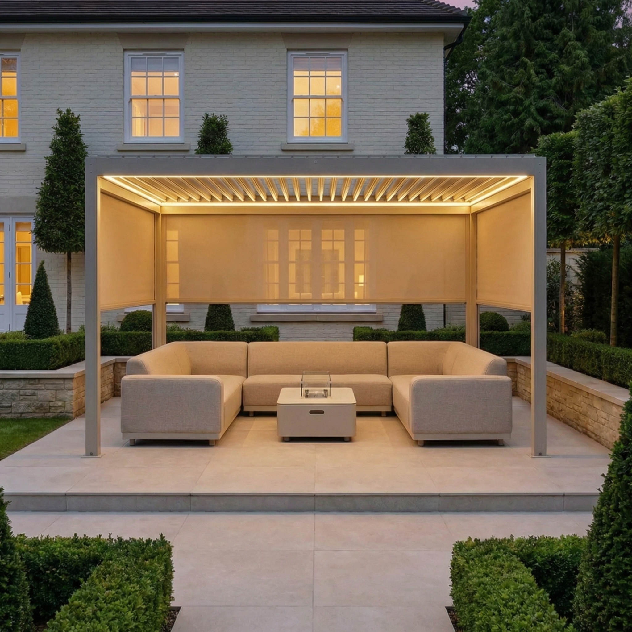 Modern outdoor lounge featuring beige sofas under a PergoSTET Plus 3m x 4m Rectangular Pergola with three manual side blinds and LED lighting in Latte, set in a landscaped garden in front of the house.