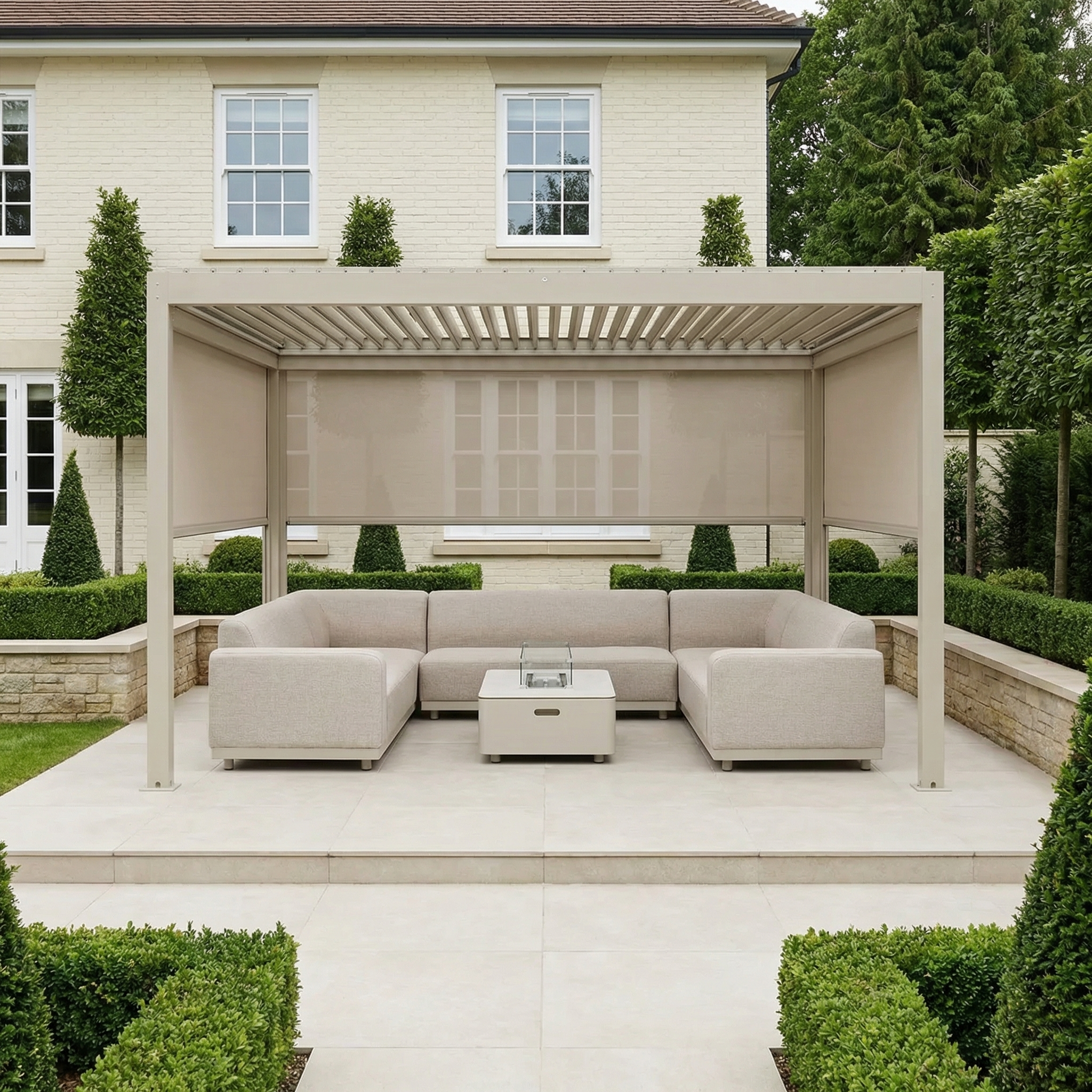 The landscaped garden patio features the PergoSTET Plus 3m x 4m Rectangular Pergola with 3 manual side blinds and LED lighting in Latte, paired with beige sofas and a fire pit table for a stylish, comfortable retreat.