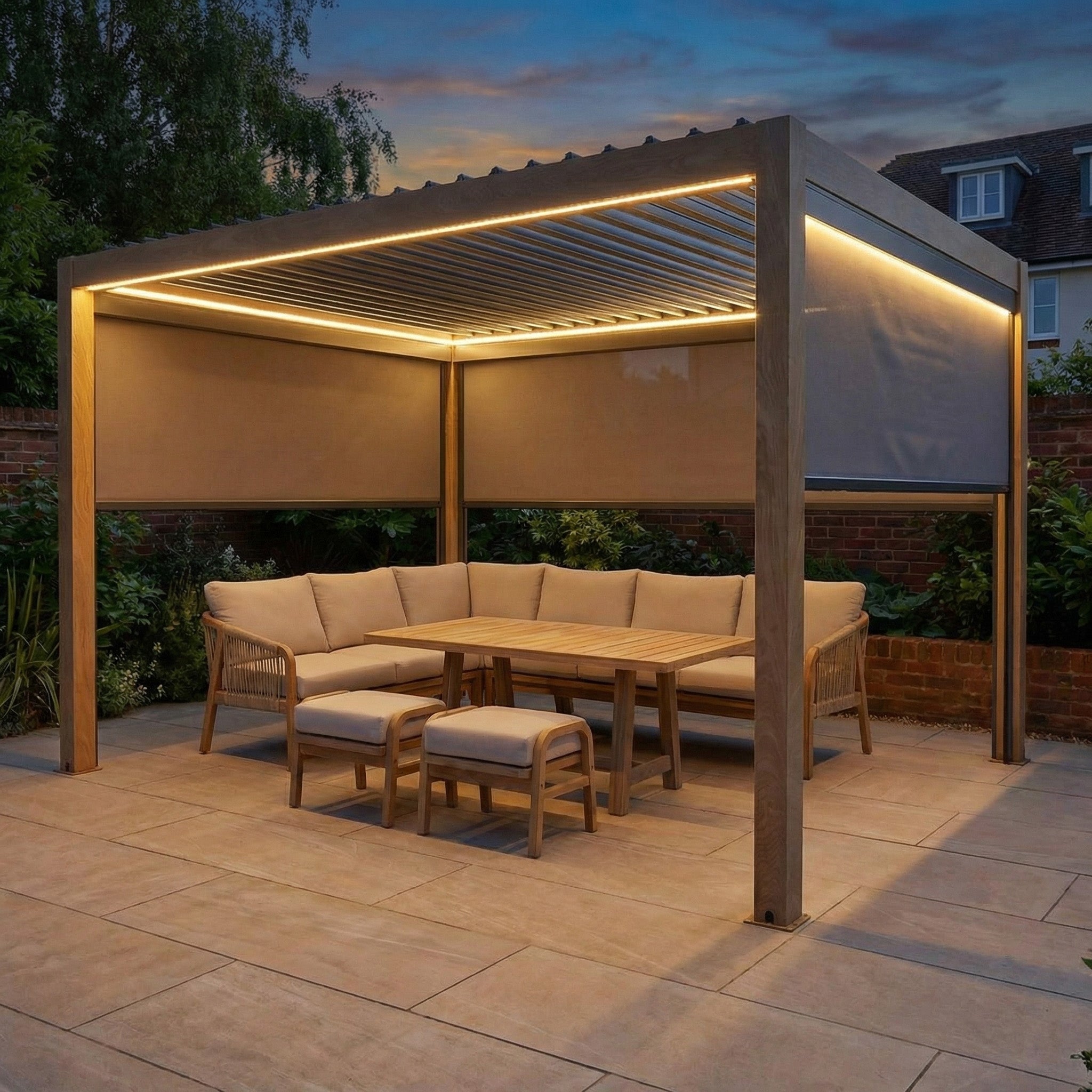 The PergoSTET Plus 3m x 4m Rectangular Pergola with wood effect, LED lighting, and three manual side blinds sits on a tiled patio at dusk with beige furniture.