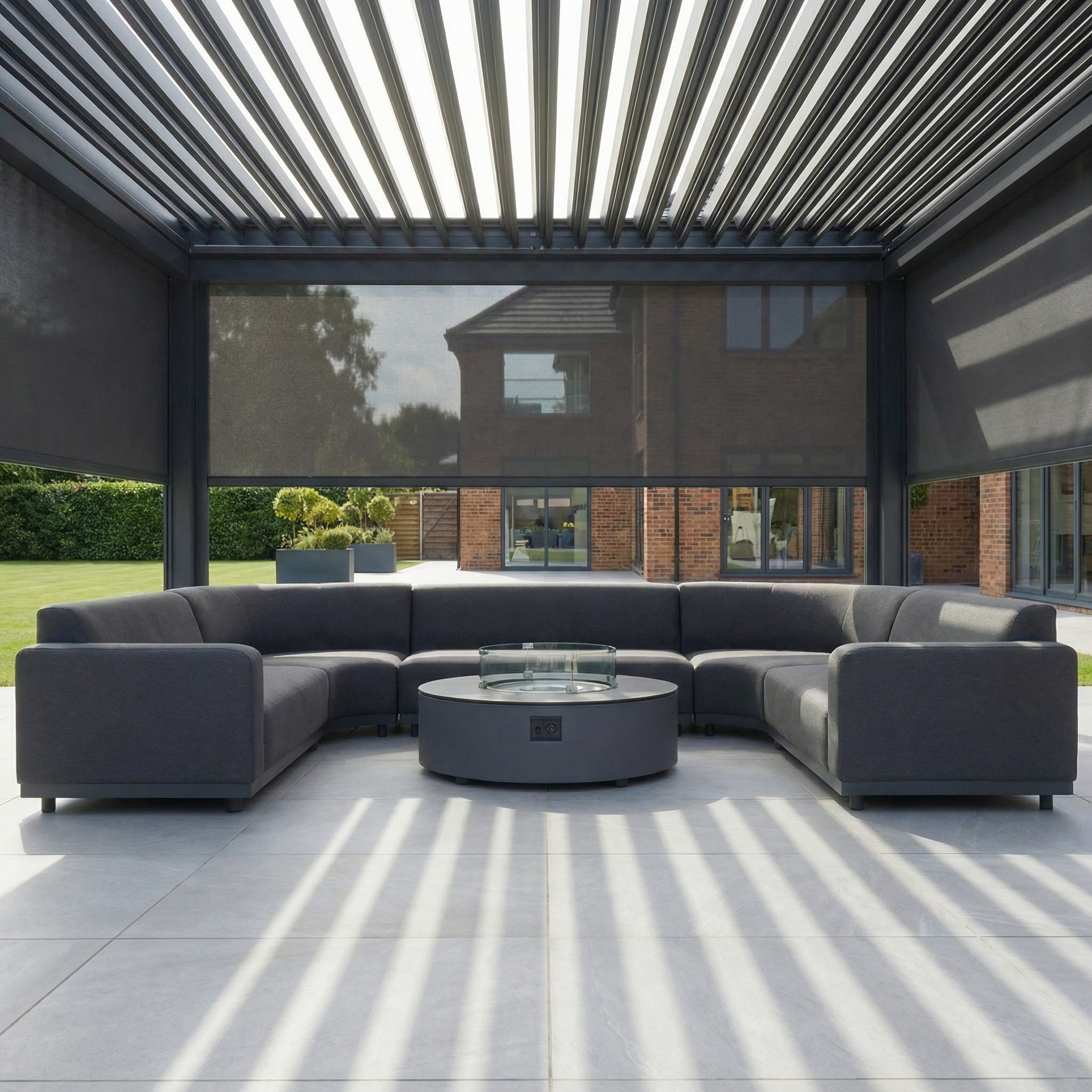 Modern outdoor patio with a gray sectional sofa, round fire pit, and a PergoSTET Plus 4m x 4m Square Pergola in Grey featuring 3 manual side blinds and LED lighting, casting striped shadows.