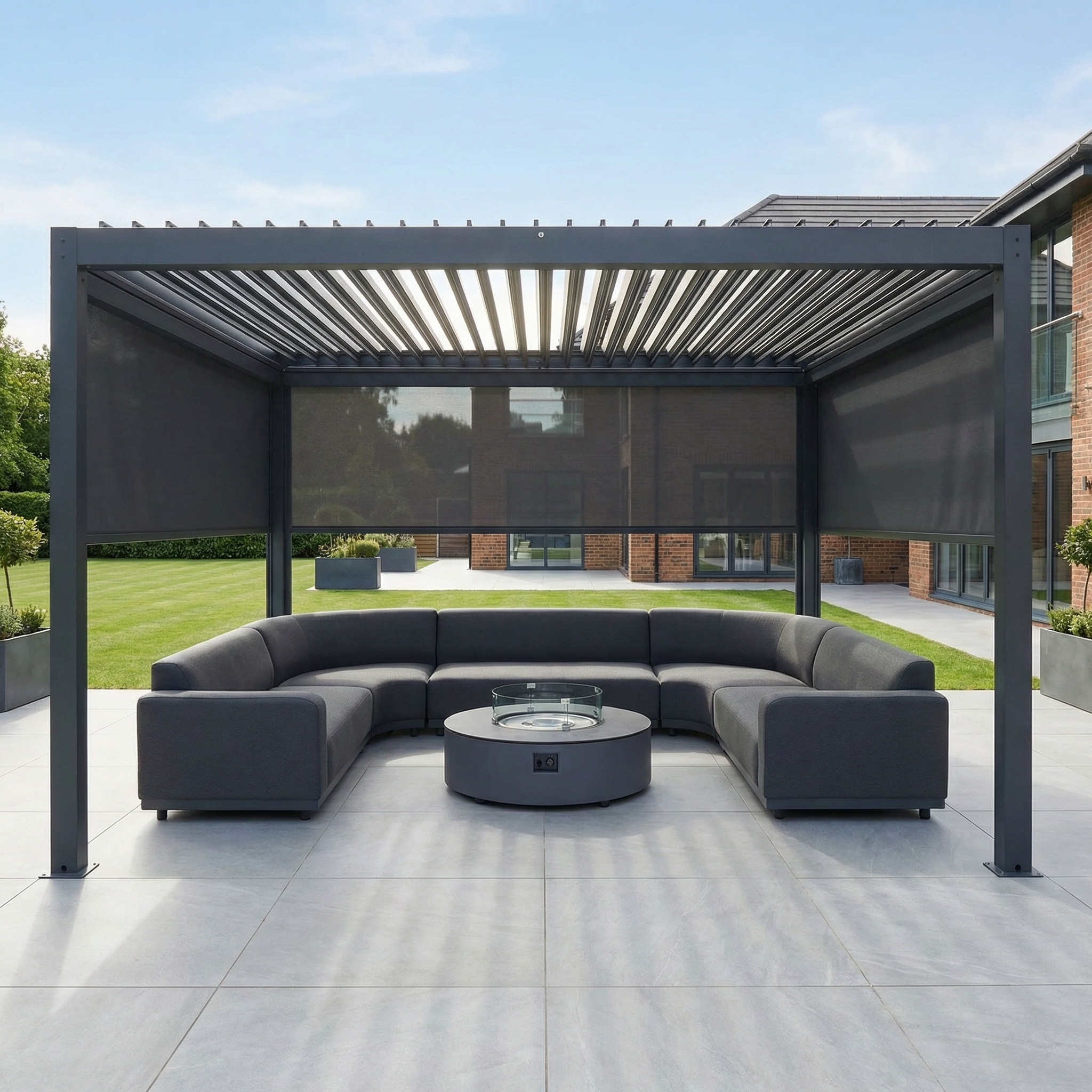 Modern outdoor patio with the 4m x 4m PergoSTET Plus Square Pergola in Grey, featuring LED lighting and 3 manual side blinds, alongside a sectional sofa and round fire pit on a spacious tiled terrace.