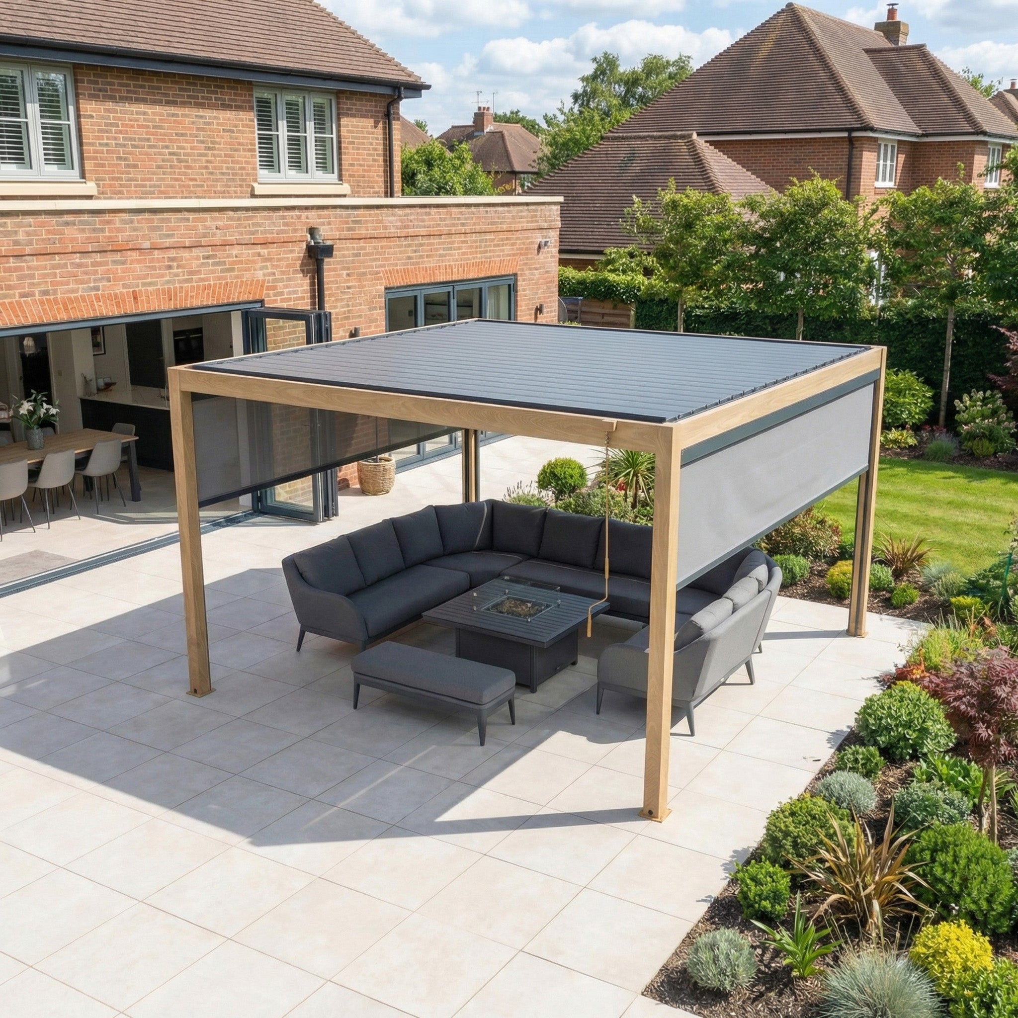 Modern patio with a sleek sectional sofa, fire pit, landscaped garden, and a stylish PergoSTET Plus 4m x 4m Square Pergola featuring 3 manual side blinds and LED lighting in wood effect for added shade and comfort.