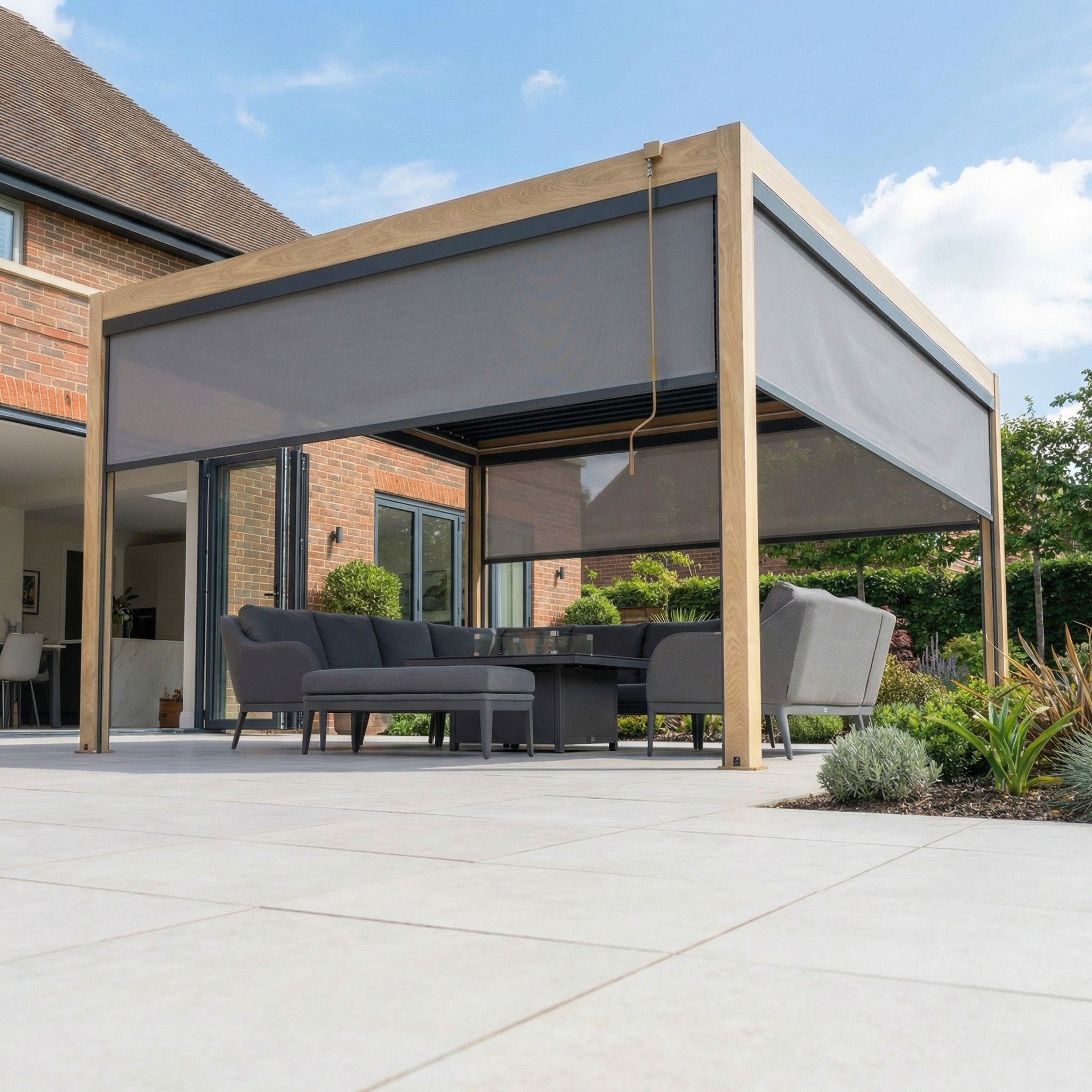 Modern outdoor patio featuring a sleek PergoSTET Plus 4m x 4m Square Pergola with wood effect, 3 manual side blinds for shade, and LED lighting, creating a comfortable seating area on sunny days.