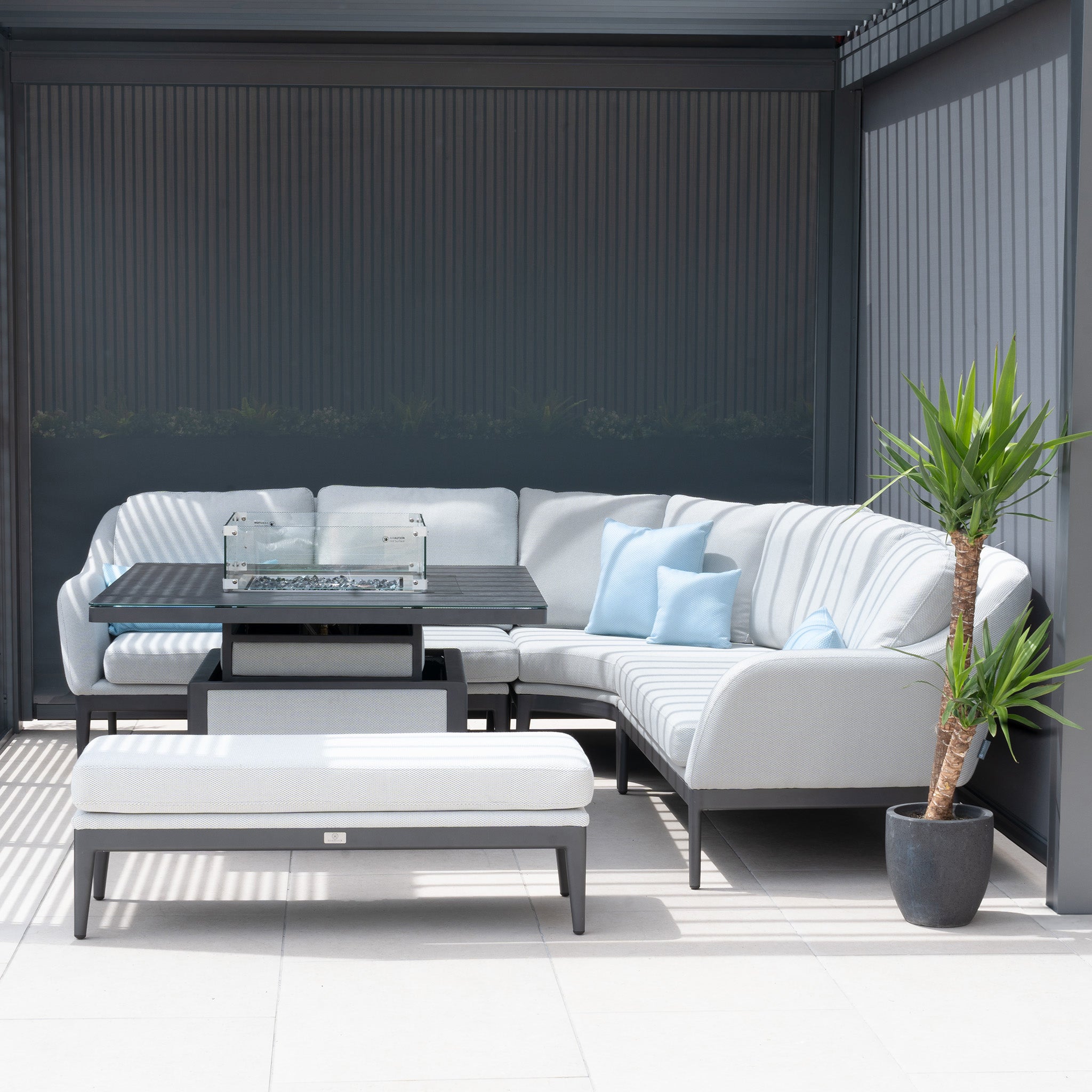 A modern outdoor patio with a gray sectional sofa, fire table, potted plant, and tiled floor under sleek PergoSTET Deluxe 3m x 6m Rectangular Pergola with motorized LED louvres and four manual side blinds in grey.
