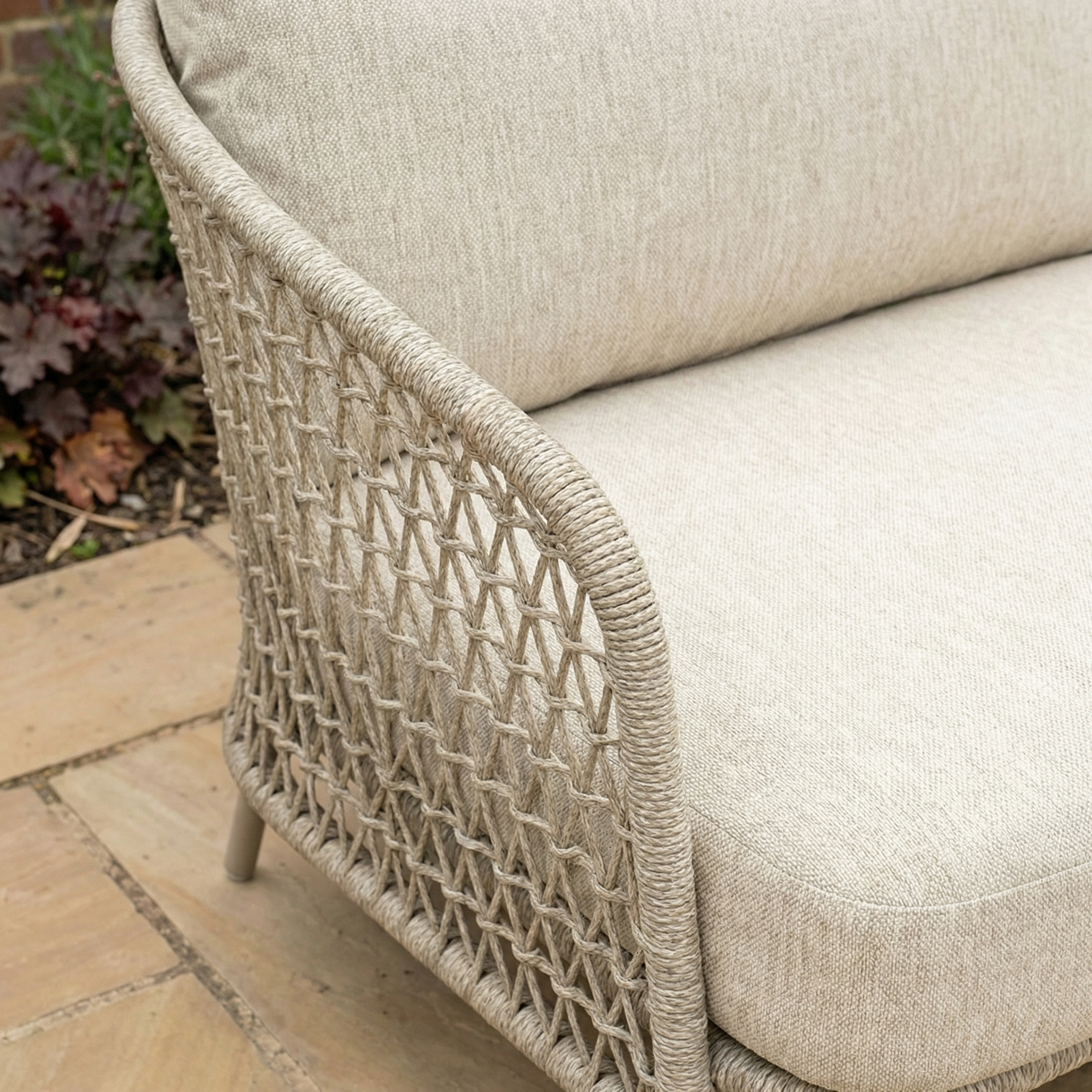 Close-up of the Puccini 3 Seat Sofa (Ex Display) in beige with woven rattan armrest, showcased on a stone patio.