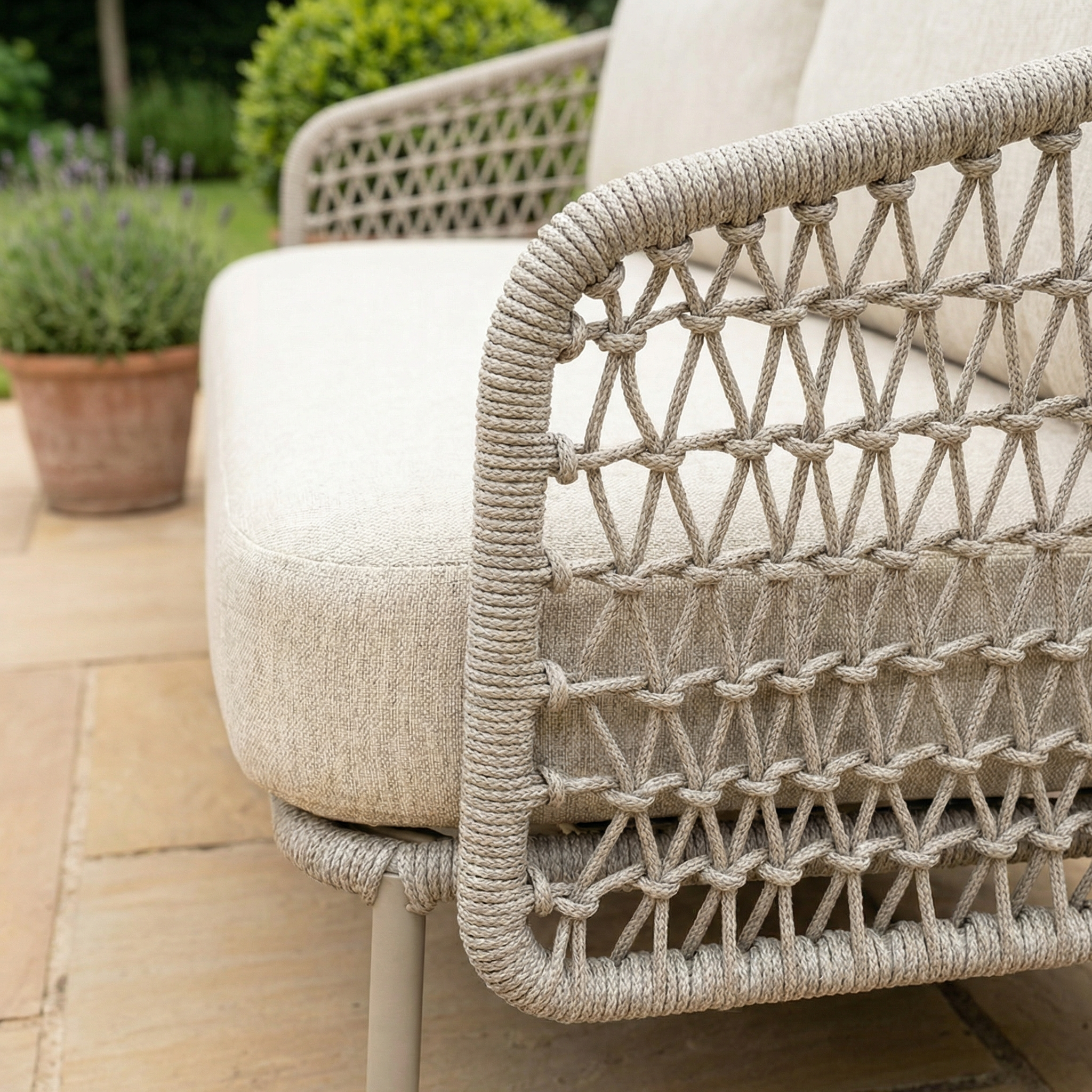 Close-up of the Puccini 3 Seat Sofa (Ex Display) featuring woven rope armrests on a stone patio, with a potted plant in the background.