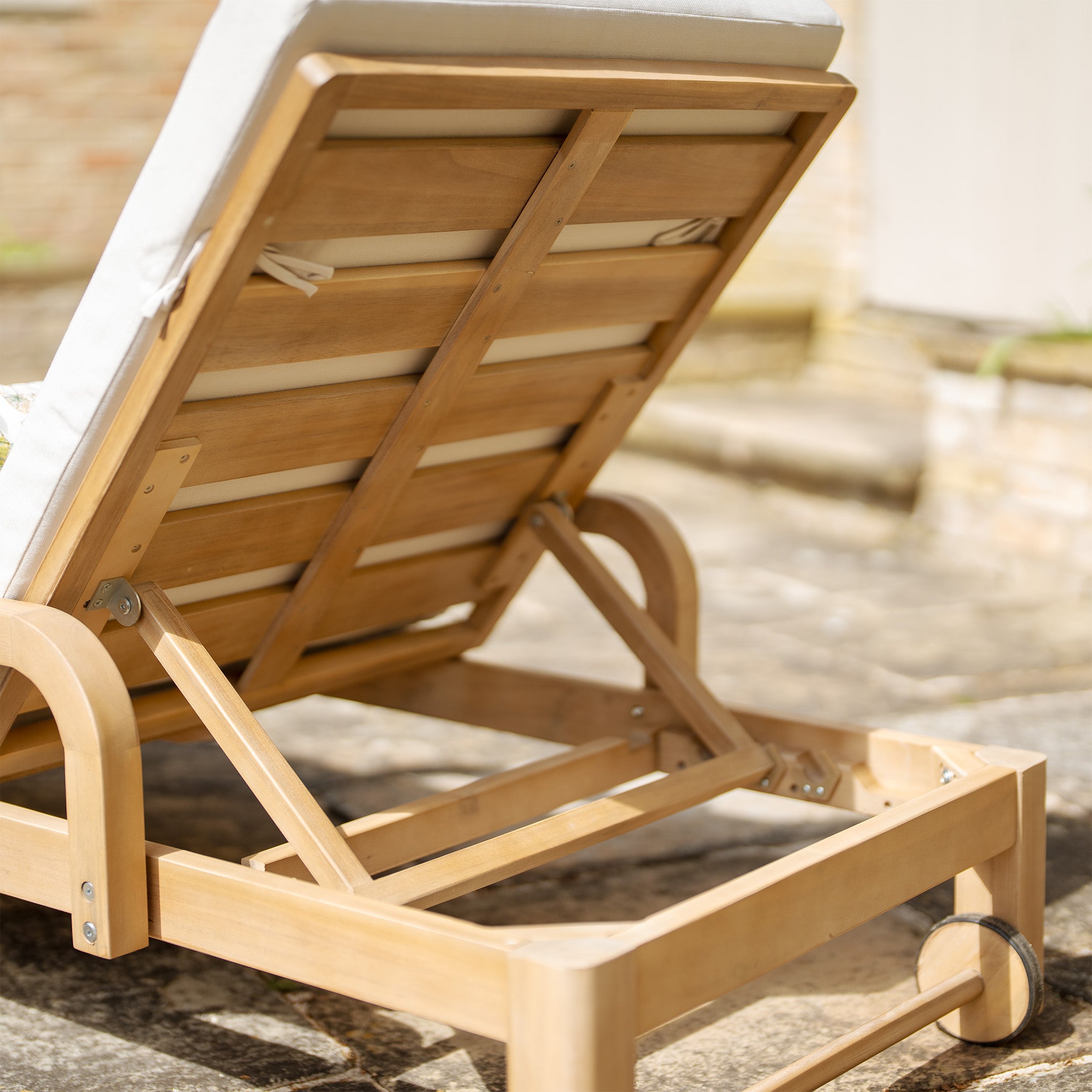 Part of the Quay collection, the Quay Sun Lounger in Linen features an acacia wood frame and a white cushion facing away, showcasing its adjustable backrest mechanism on a stone patio—perfect for sun-lounging.