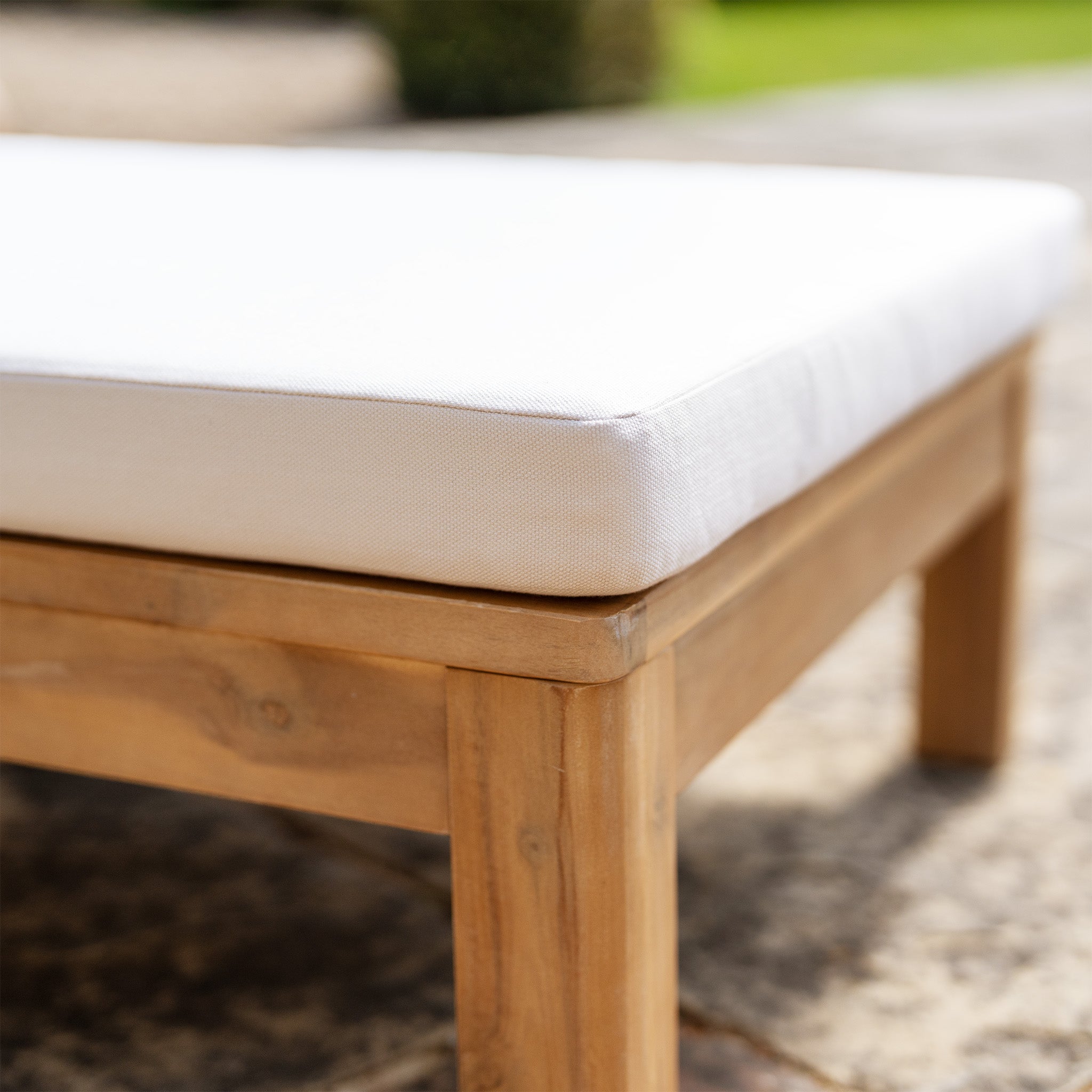 Close-up of the Quay Sun Lounger in Linen, showcasing its acacia wood frame and white cushion, positioned on a tiled patio with a softly blurred backdrop of lush greenery.