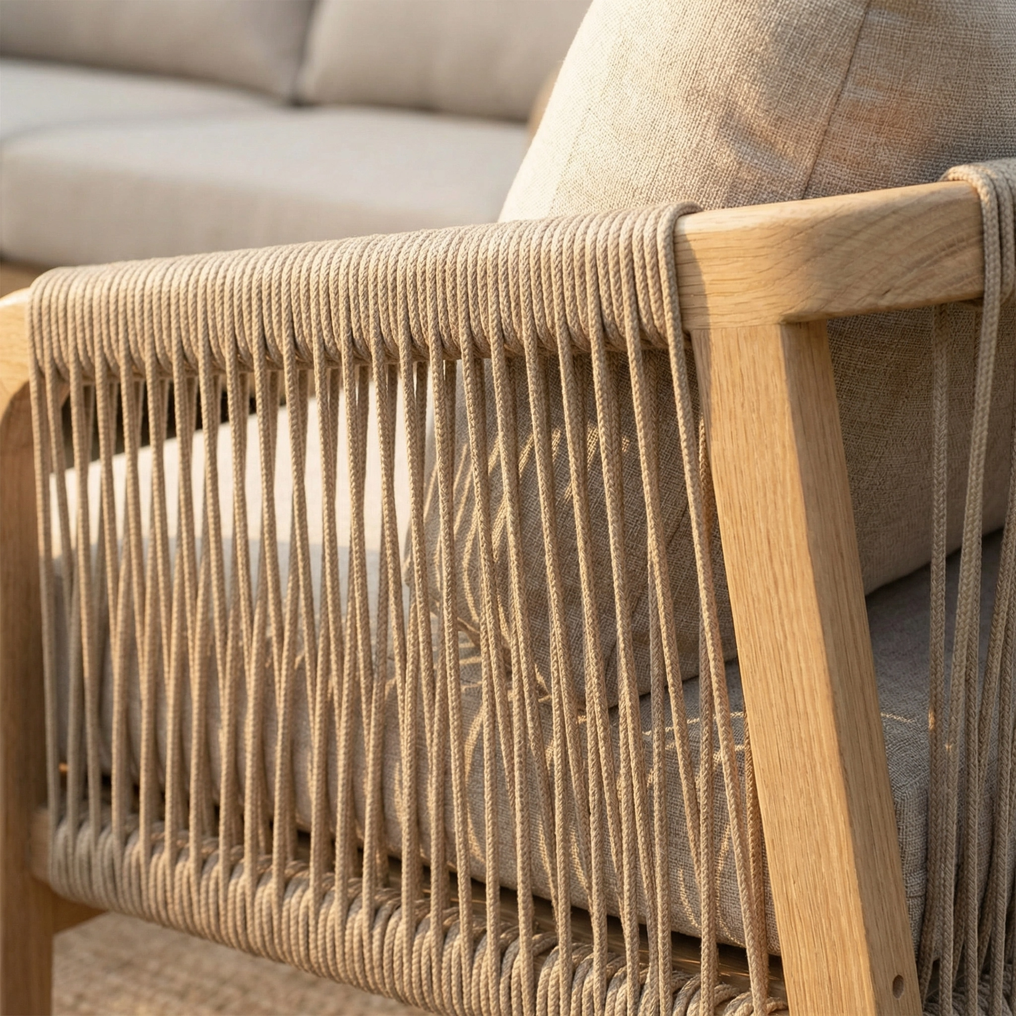 Close-up of a wooden chair with beige rope detailing and a light cushion, part of an elegant outdoor lounge set, with the Quay 3 Seat Sofa Set in Mocha visible in the background.