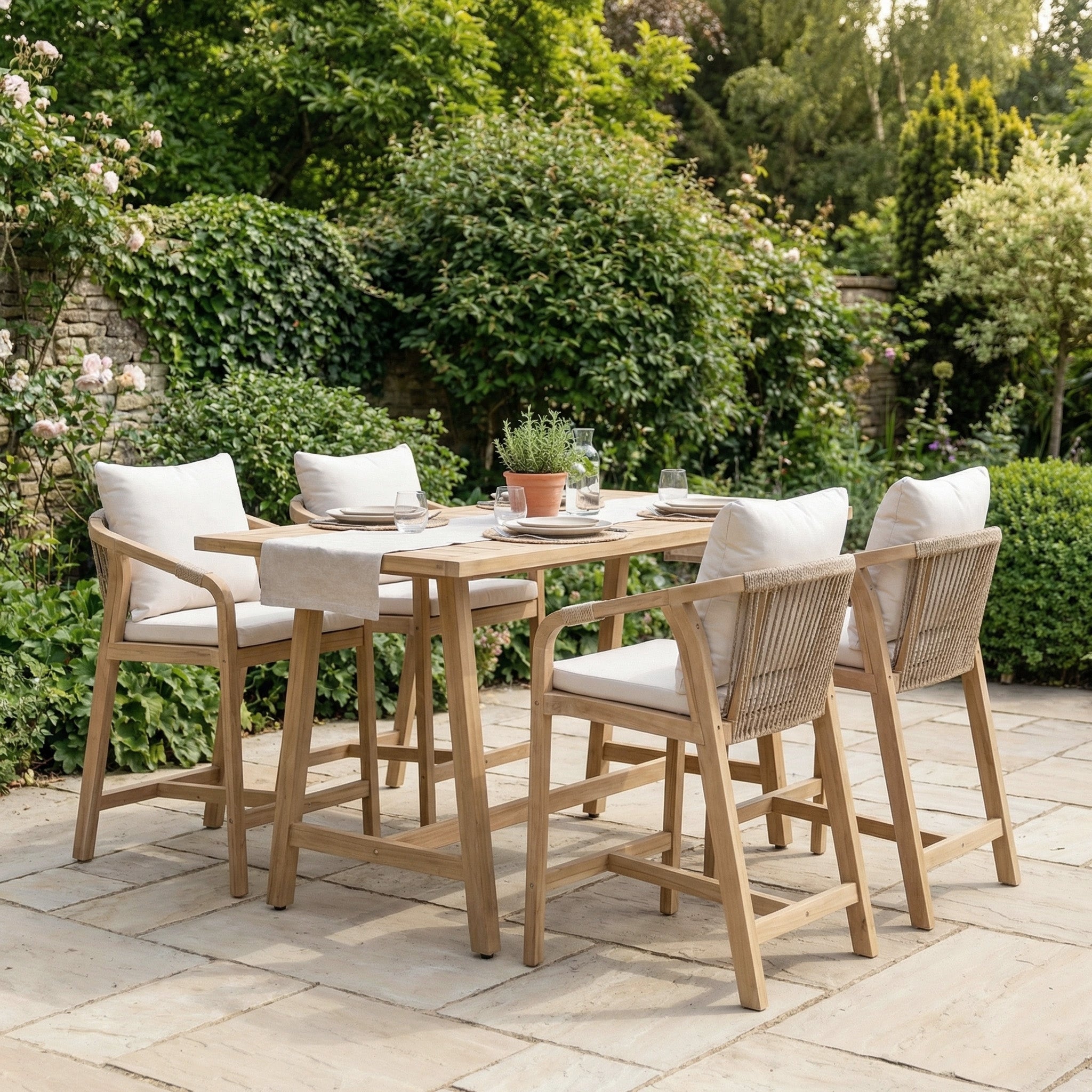 The Quay 4 Seat Rectangular Bar Set in Linen, featuring cushioned chairs, is ideal outdoor furniture for relaxing alfresco dining on your patio amid lush garden greenery.