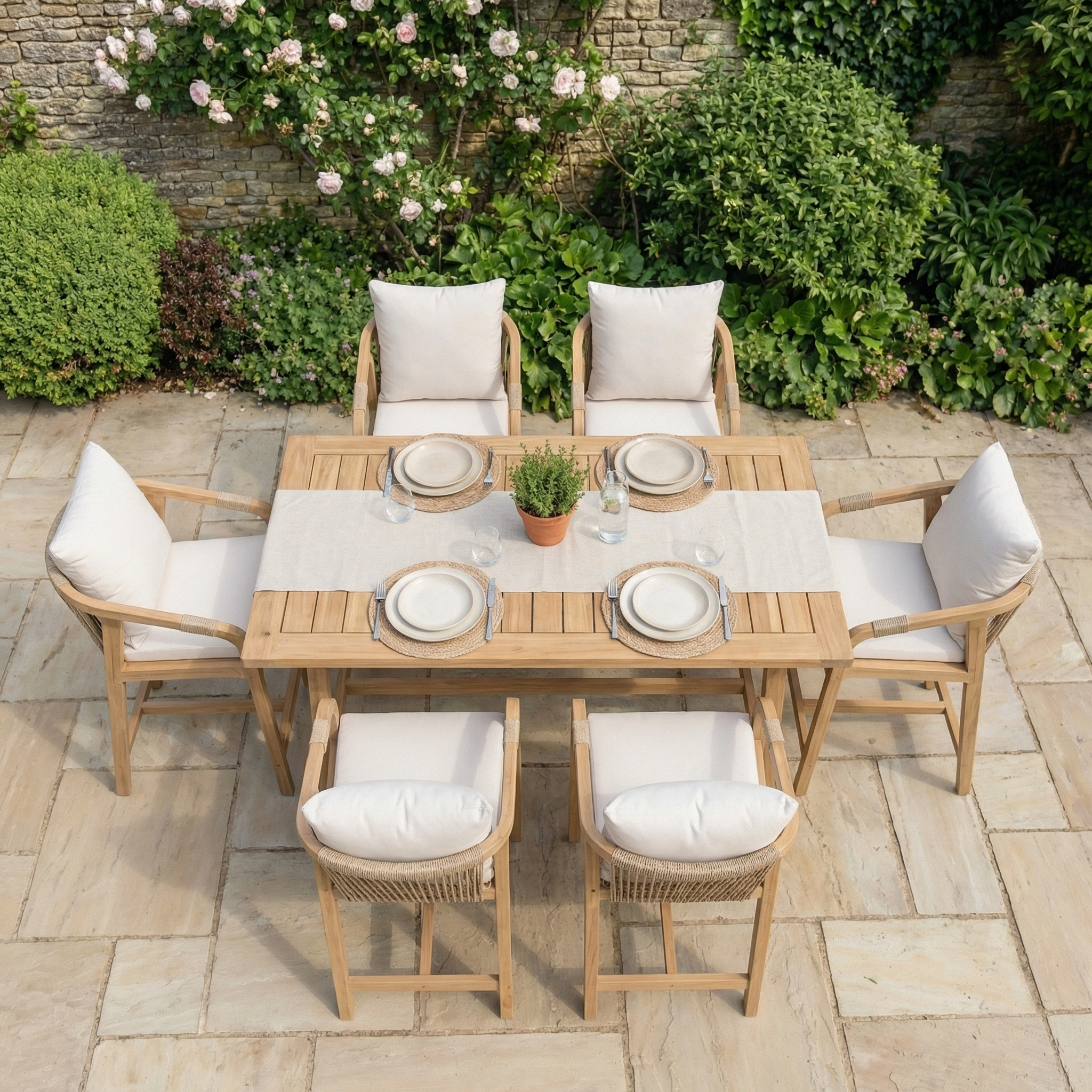 The Quay 4 Seat Rectangular Bar Set in Linen features a stylish wooden design with comfy white cushions, perfect for outdoor dining on a stone patio surrounded by greenery.