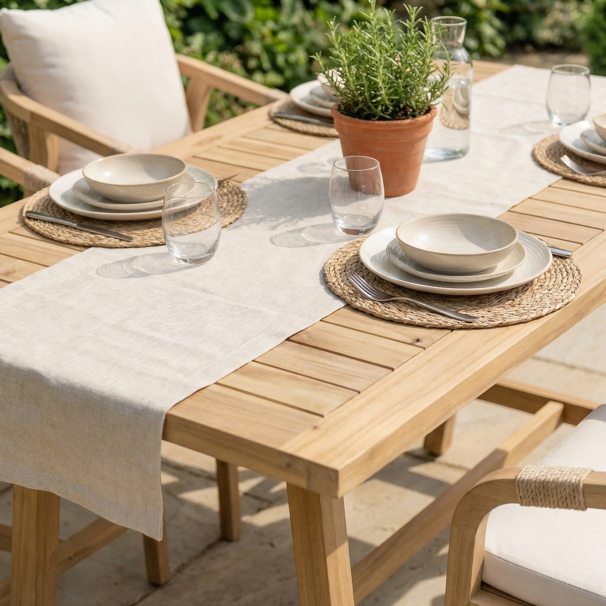 The Quay 6 Seat Rectangular Bar Set in Linen features an acacia wood table, complete with plates, glasses, and a potted herb centerpiece on a sunny patio.