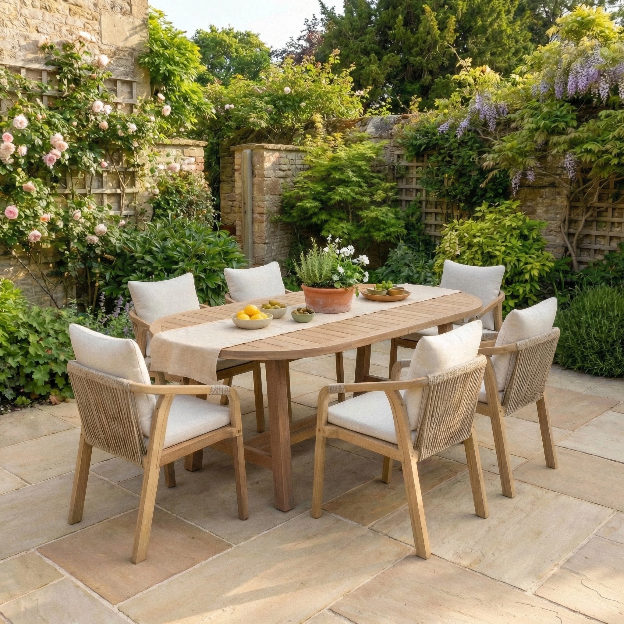 The Quay 6 Seat Oval Dining Set in Linen is perfect for stylish acacia garden furniture lovers, offering inviting outdoor dining for six on your patio amid lush greenery and flowers.