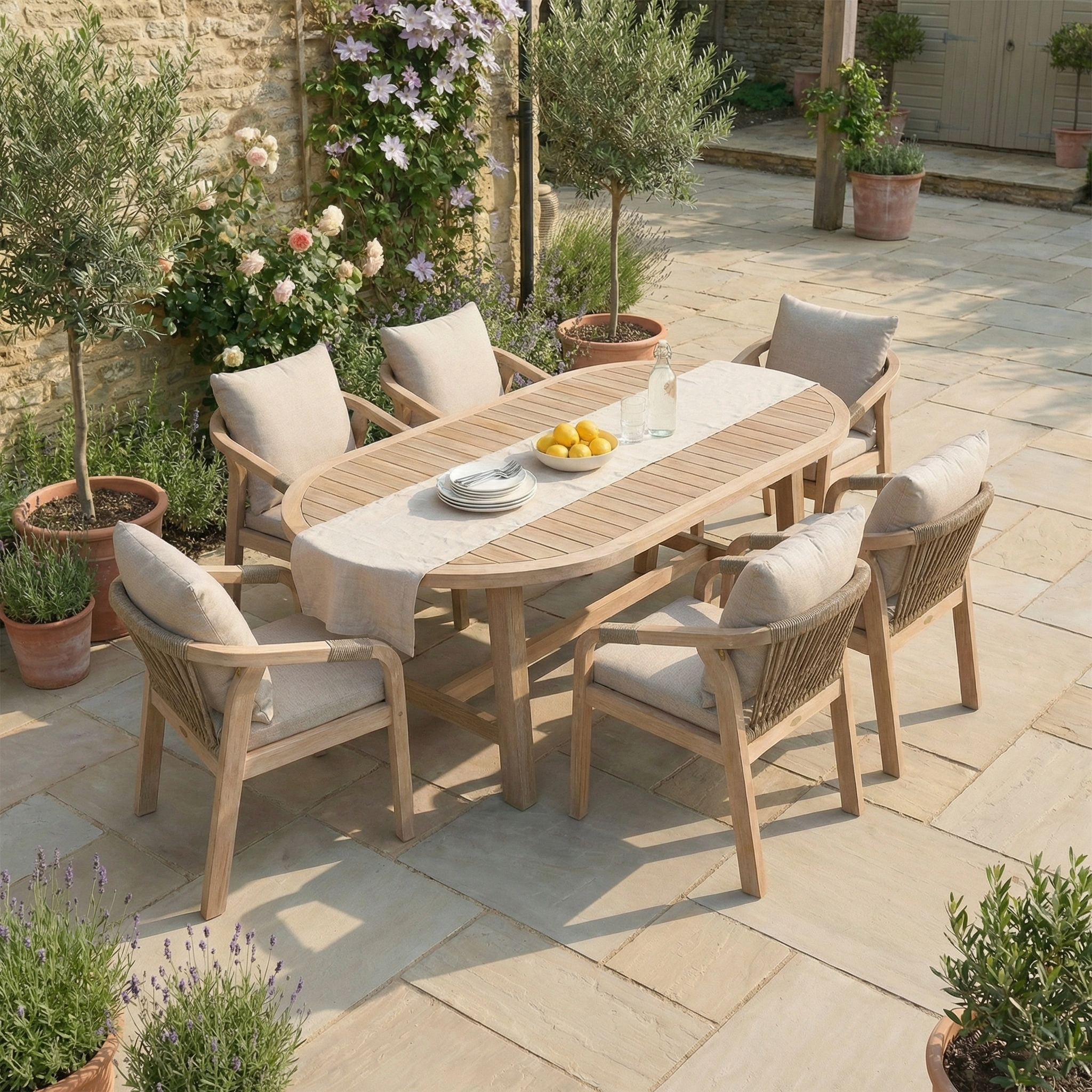 Quay 6 Seat Oval Dining Set in Mocha: This wooden outdoor dining table includes six cushioned chairs and is styled with a bottle, glasses, and lemons arranged on top.