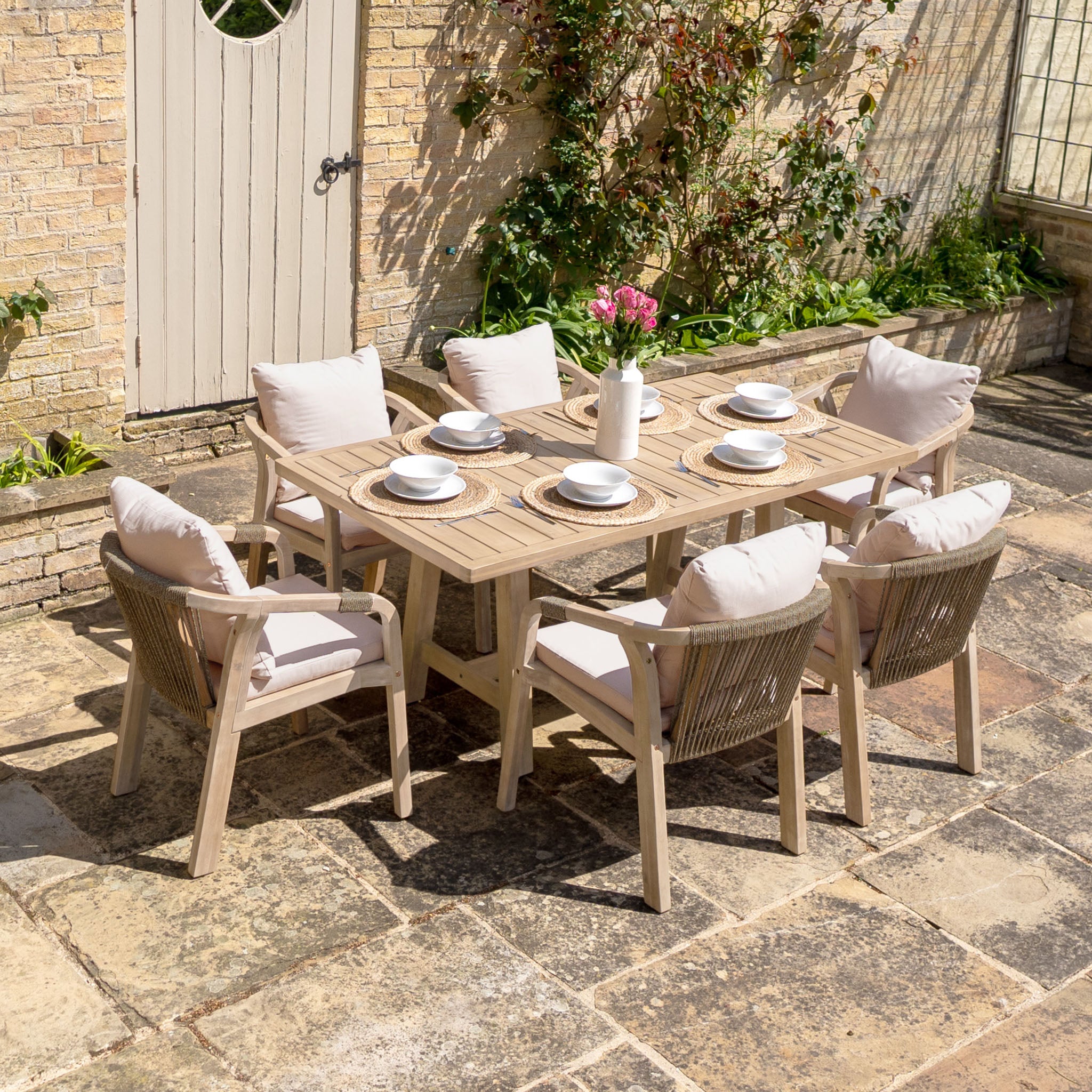 The Quay 6 Seat Rectangular Dining Set in Mocha features a eucalyptus frame table and six cushioned chairs, accented with flowers—bringing style and comfort to your outdoor furniture collection.