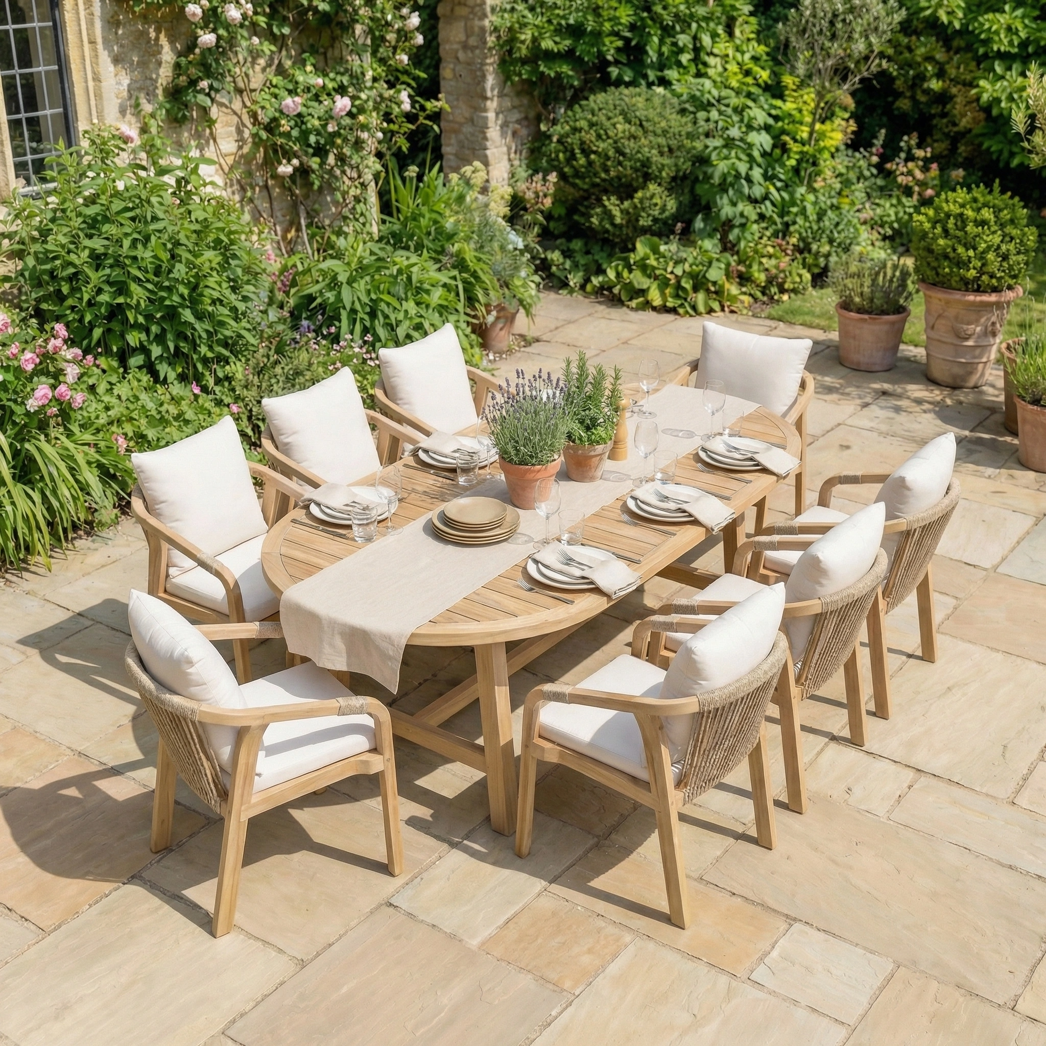 The Quay 8 Seat Oval Dining Set in Linen includes cushioned chairs and is shown styled with tableware and potted plants on a stone patio, perfect for outdoor dining.