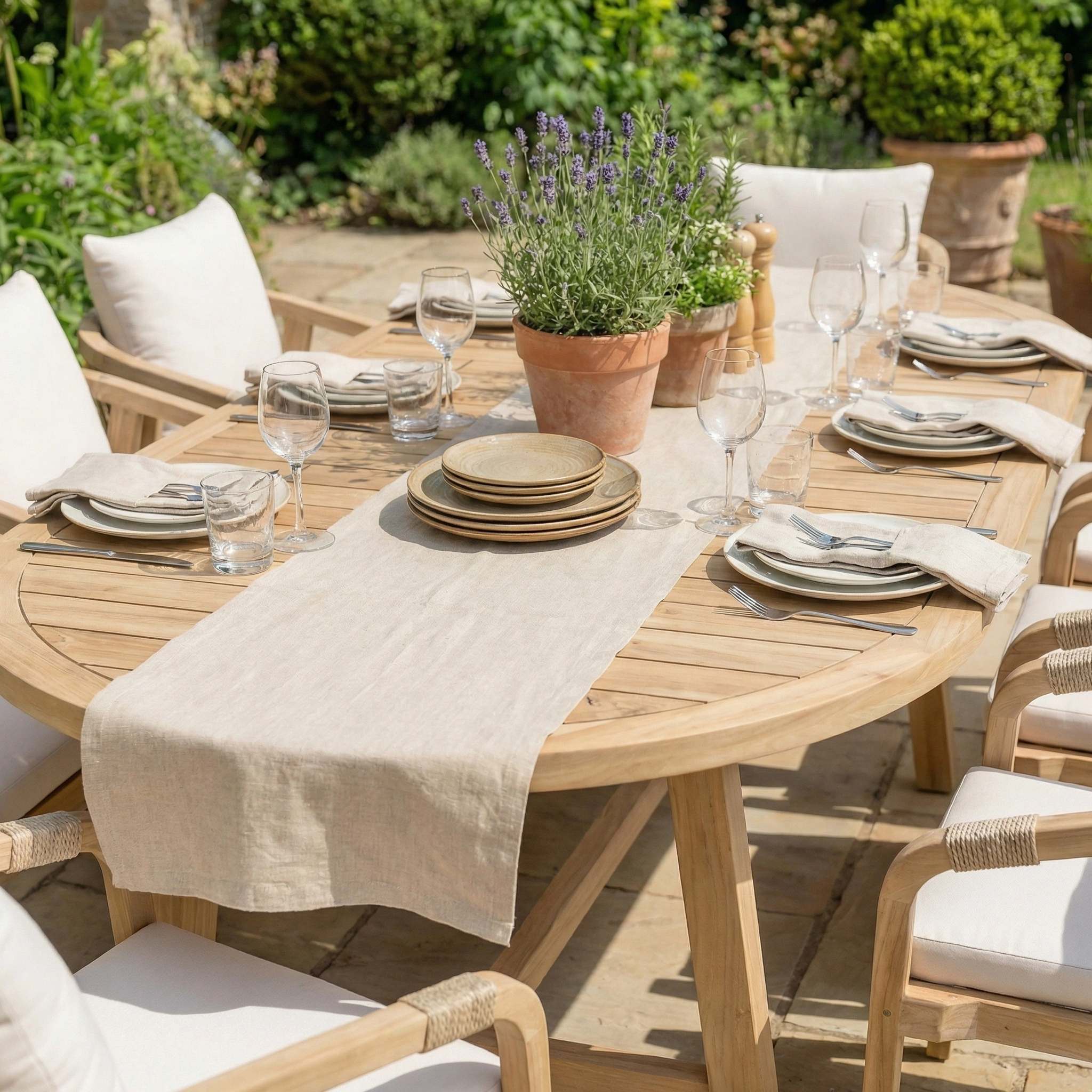 The Quay 8 Seat Oval Dining Set in Linen, featuring a wooden oval table arranged with plates, glasses, and a potted lavender centerpiece, is perfect for outdoor gatherings and elegant alfresco dining.