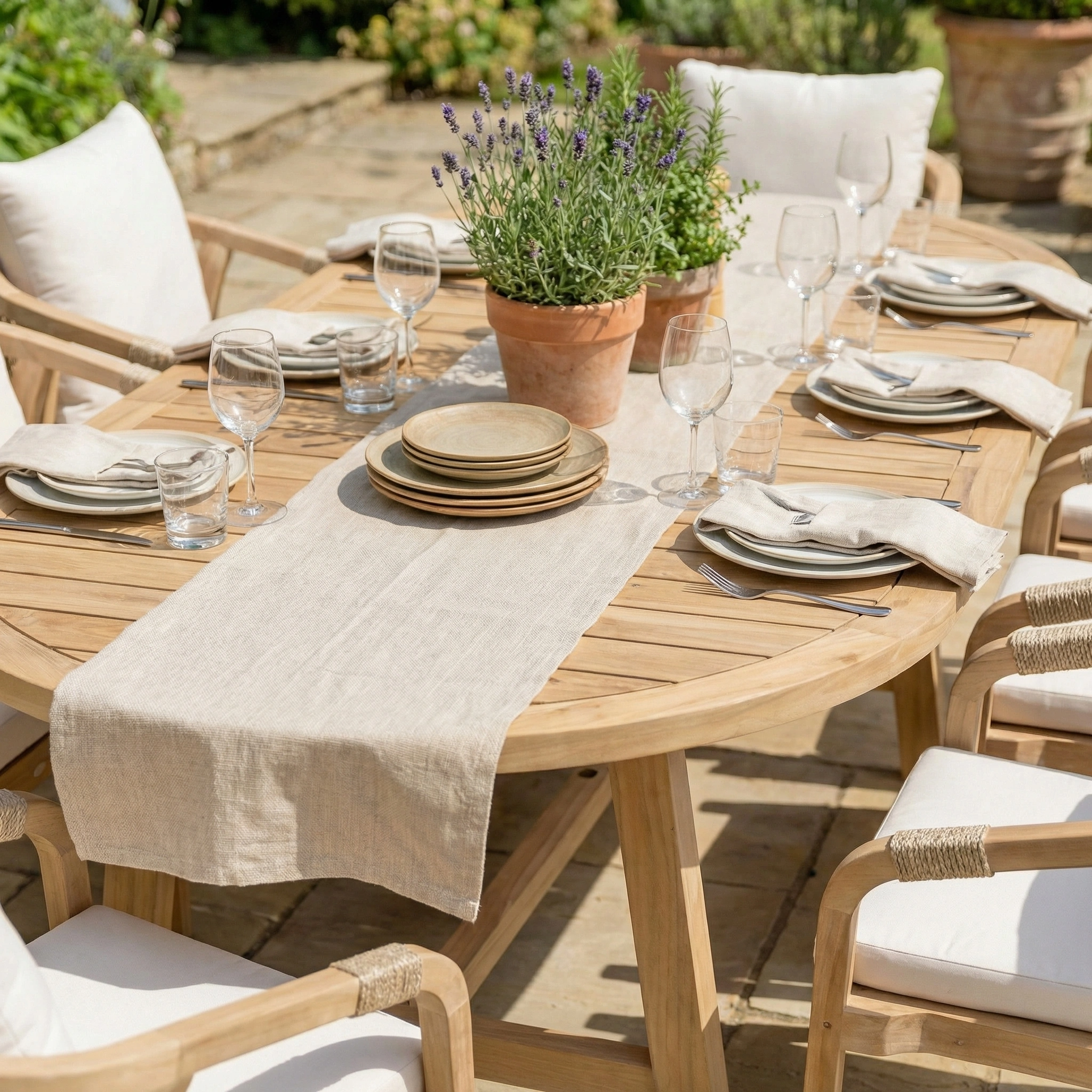 The Quay 8 Seat Oval Dining Set in Linen, arranged with plates, glasses, napkins, and a potted lavender centerpiece, offers elegant outdoor dining for any gathering.