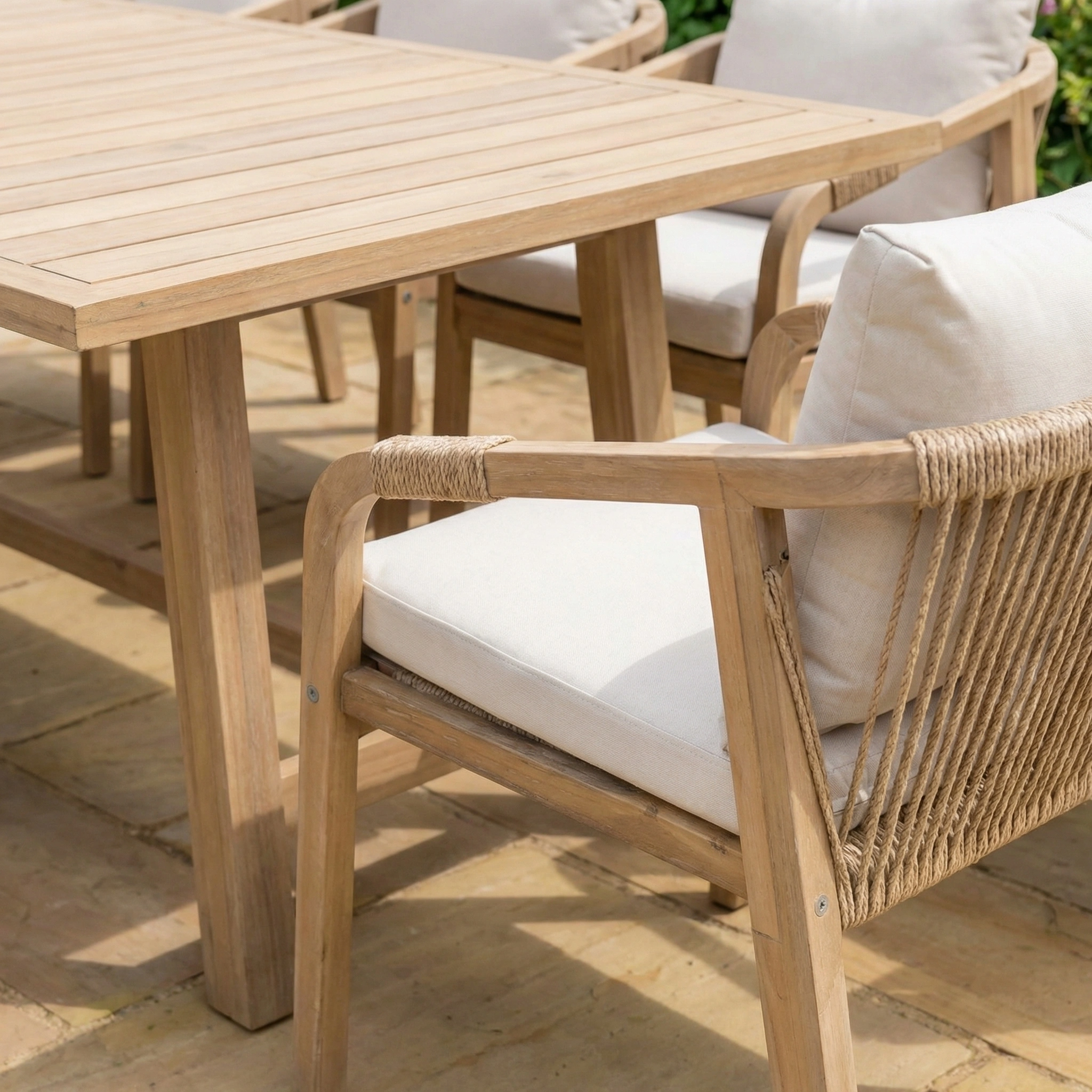 The Quay 8 Seat Rectangular Dining Set in Linen includes cushioned chairs and an acacia wood table, perfect for enjoying meals on a sunlit stone patio.