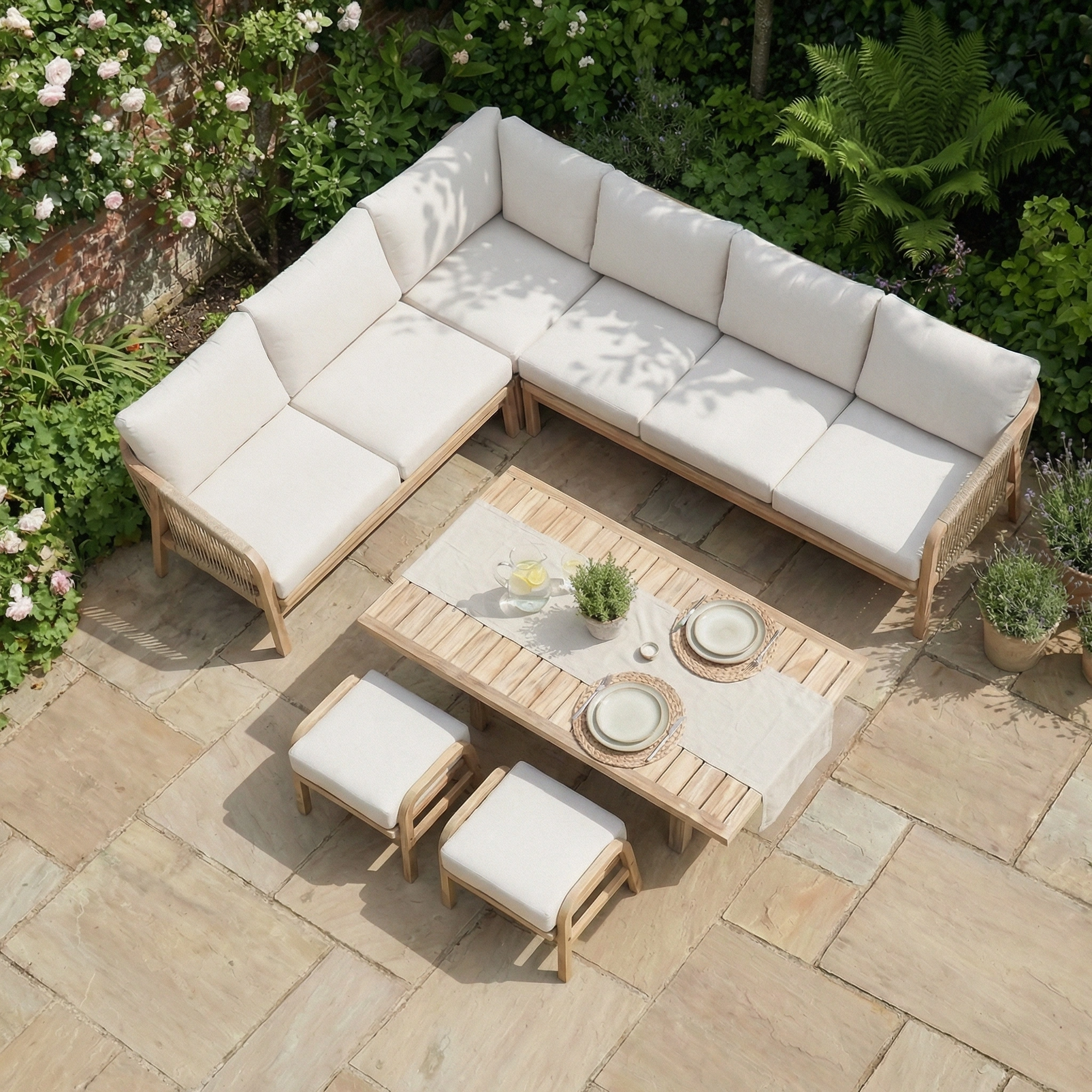 Aerial view of the Quay Corner Dining Set in Linen, featuring cream cushions, an acacia wood dining table, two stools, and lush surrounding greenery.