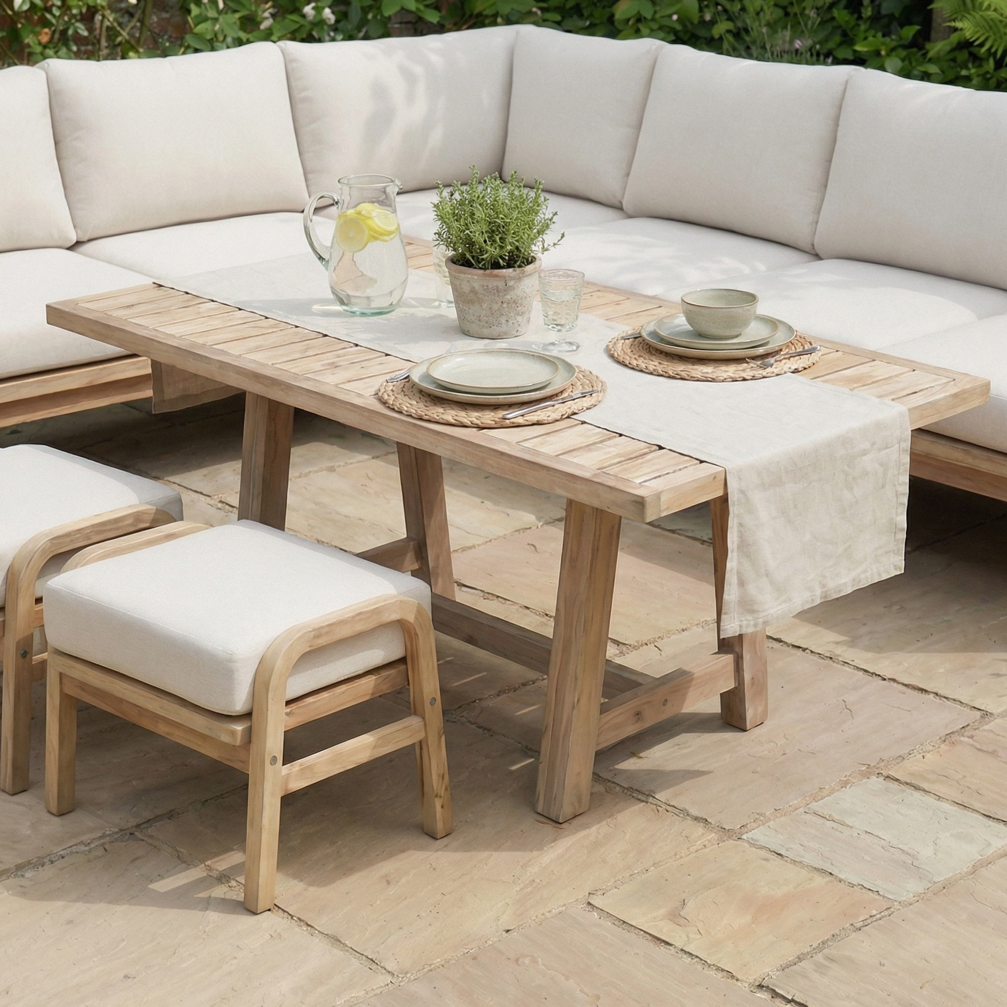 The Quay Corner Dining Set in Linen is arranged for casual dining, featuring lemonade, potted plants, and cozy cushioned seating.