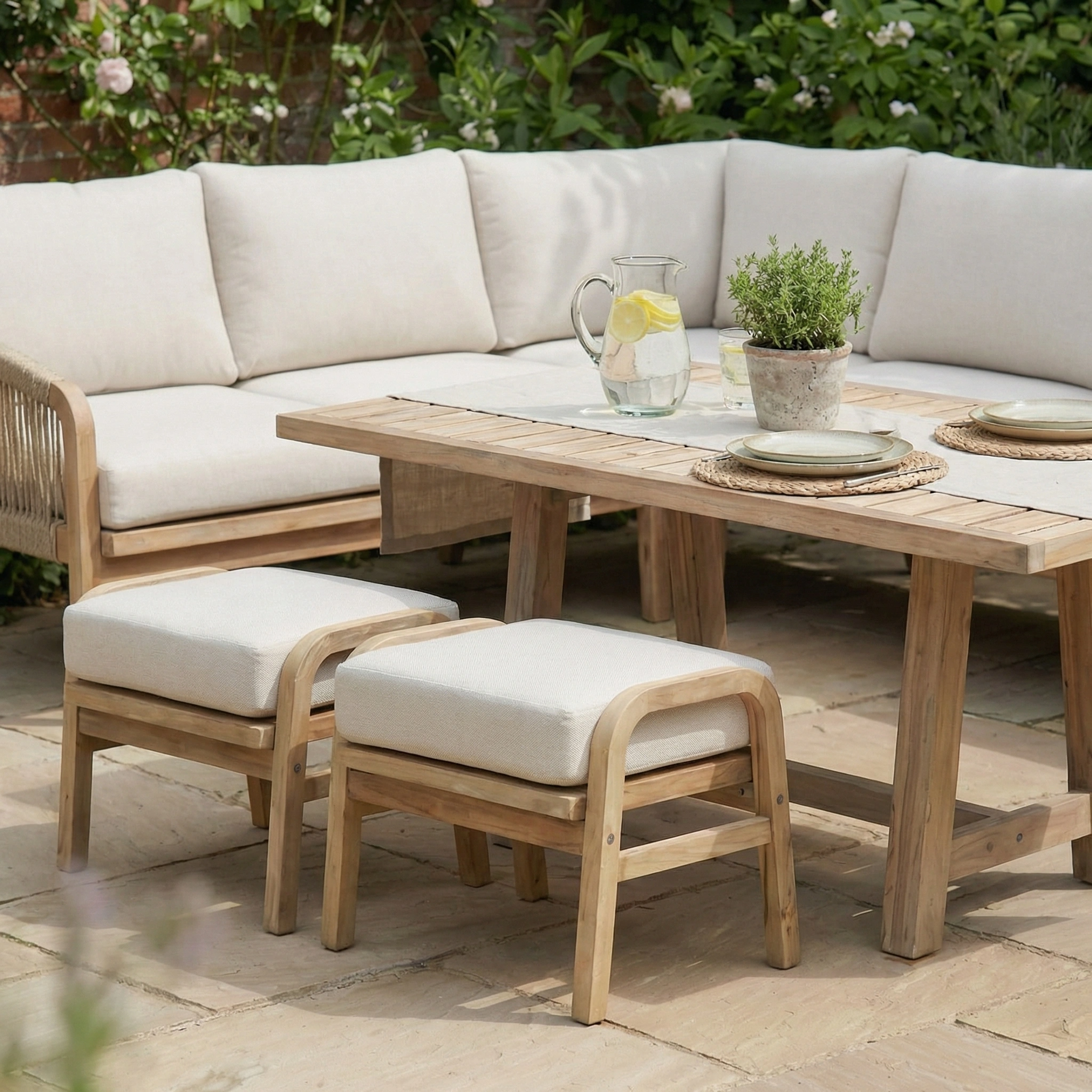 The Quay Corner Dining Set in Linen features durable acacia wood, beige cushions, a table, two plates, and a pitcher—ideal for relaxed outdoor gatherings.