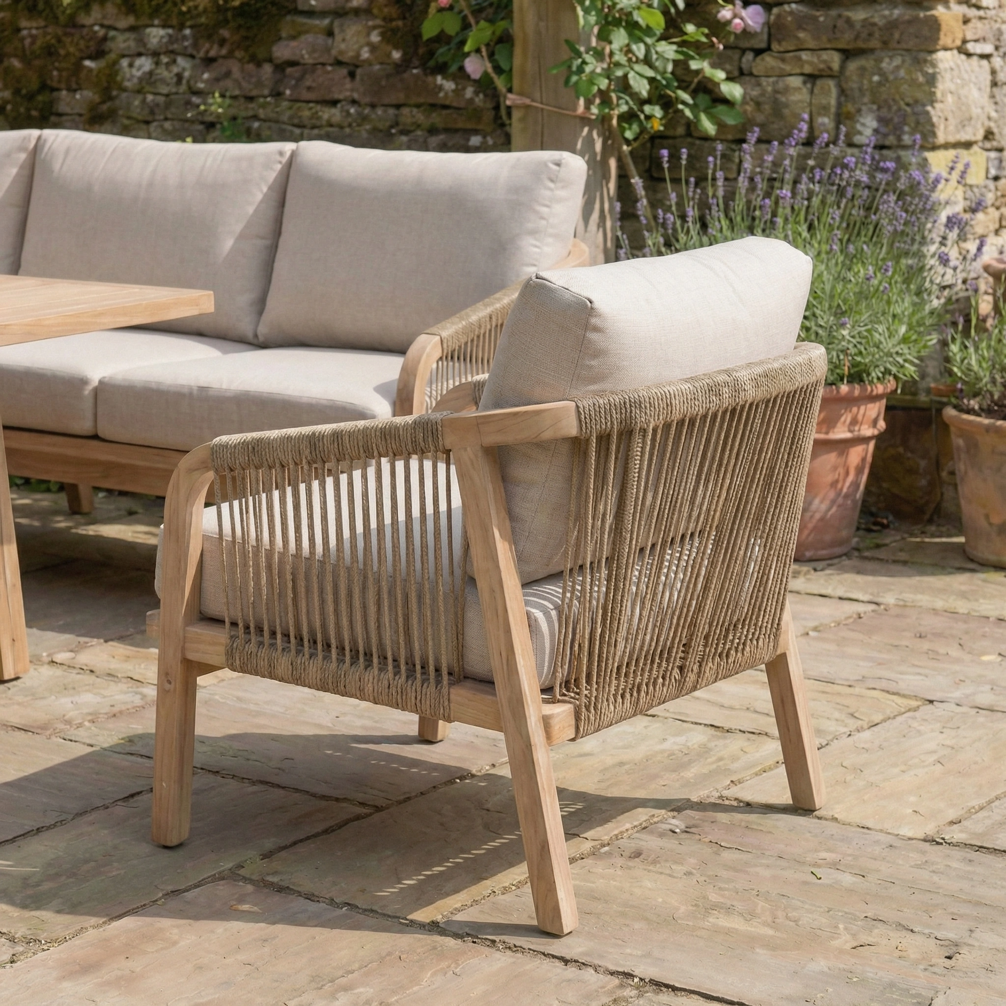 The Quay Corner Dining Set with Armchair in Mocha features rope sides, water-resistant cushions, and eucalyptus wood, shown on a stone patio beside potted plants and matching sofa for a cohesive outdoor look.