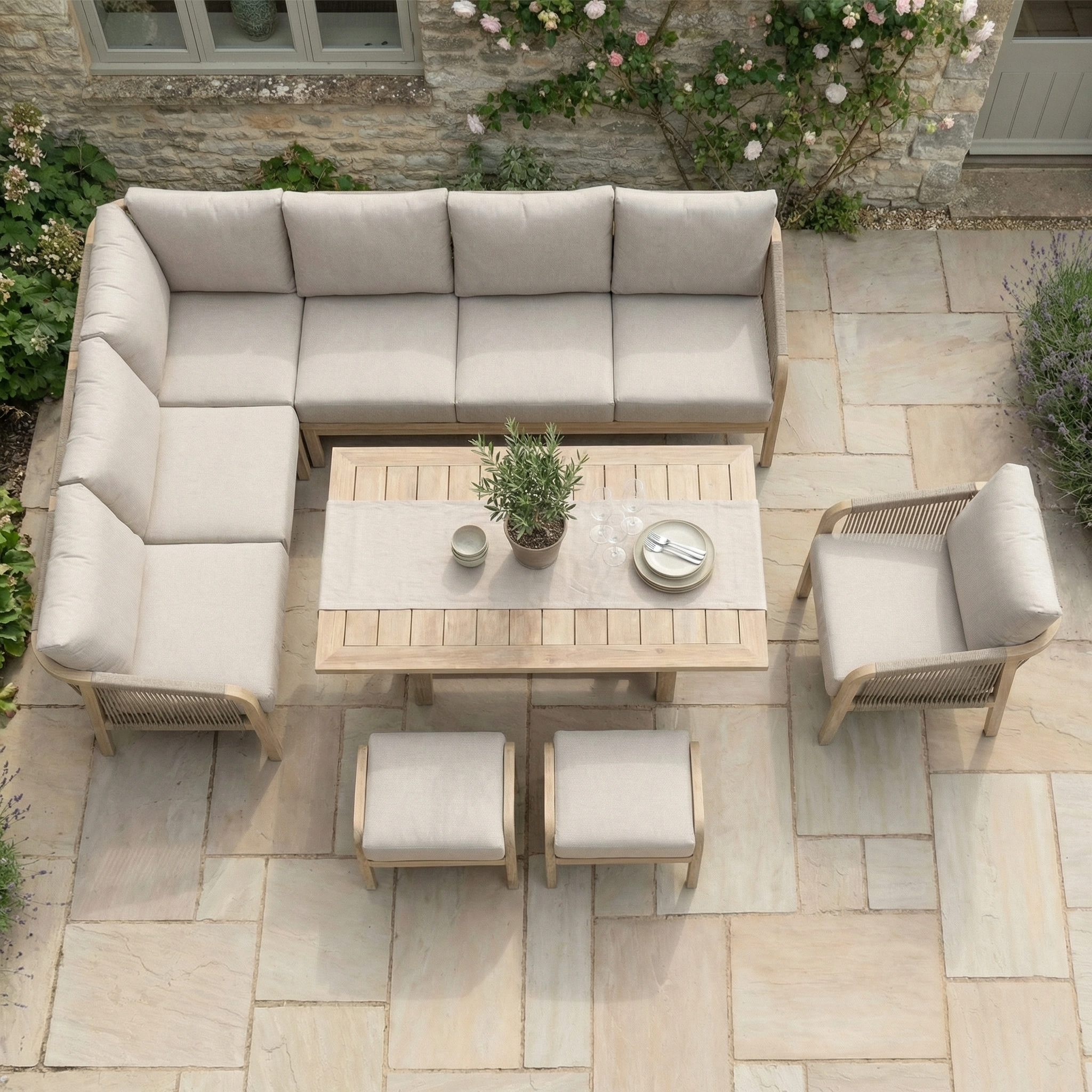 The Quay Corner Dining Set with Armchair in Mocha features water-resistant cushions and a sturdy eucalyptus wood table, perfect for outdoor dining on a stone-tiled terrace surrounded by vibrant plants near the garden.