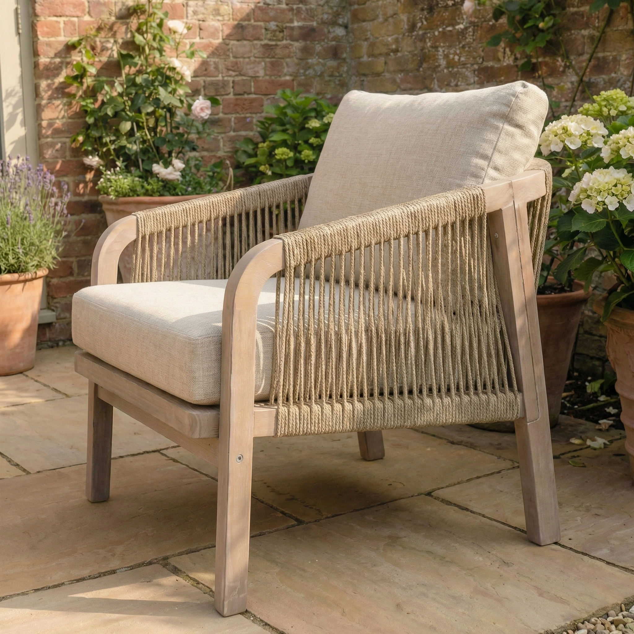 Mocha cushioned wooden garden chair with rope sides, set on a stone patio among potted plants—part of the stylish Quay Lounge Set in Mocha.