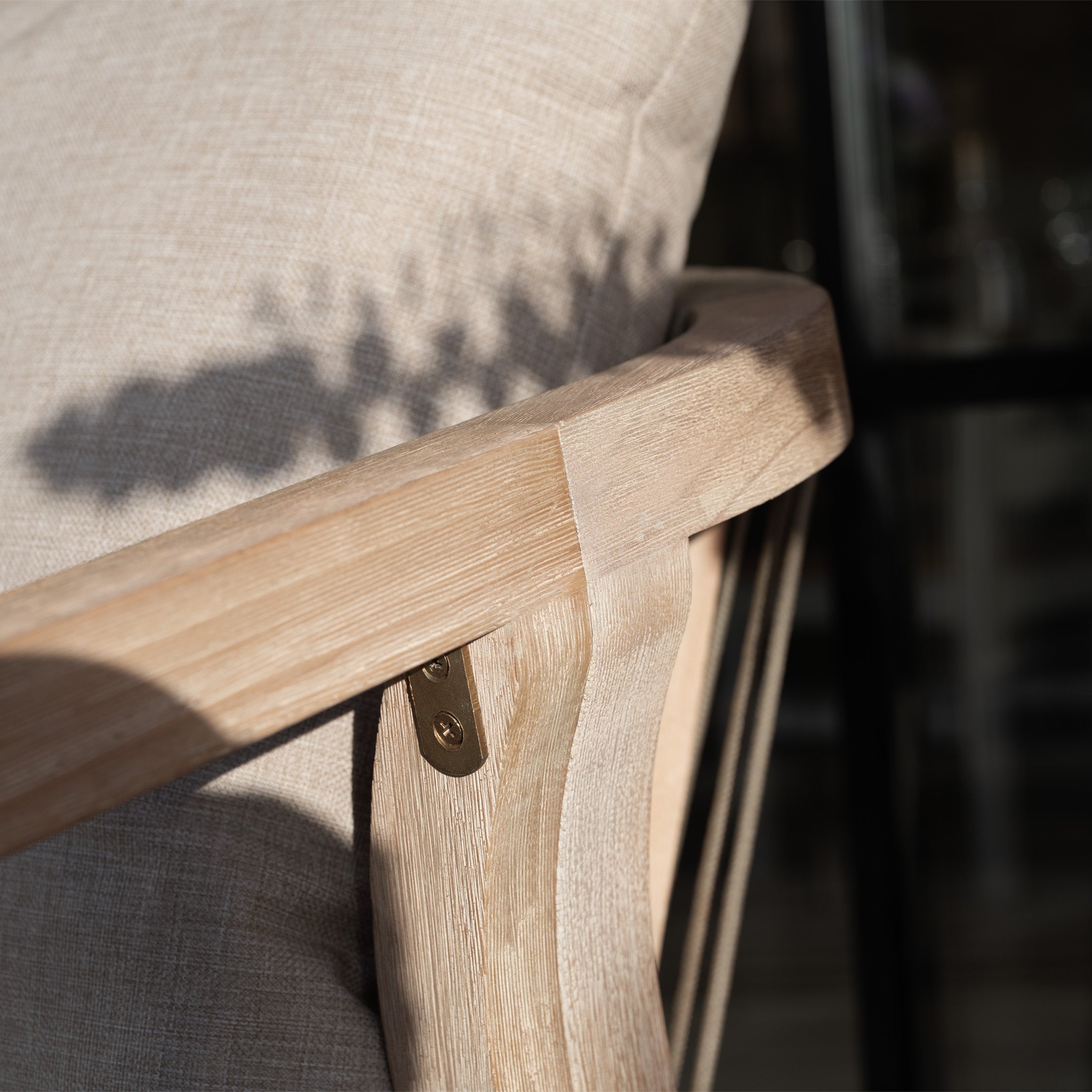 Close-up of a wooden armrest with a beige cushion, casting a plant shadow—part of the Quay Corner Sofa Dining Set in Mocha, featuring an elegant rope-weave backrest.