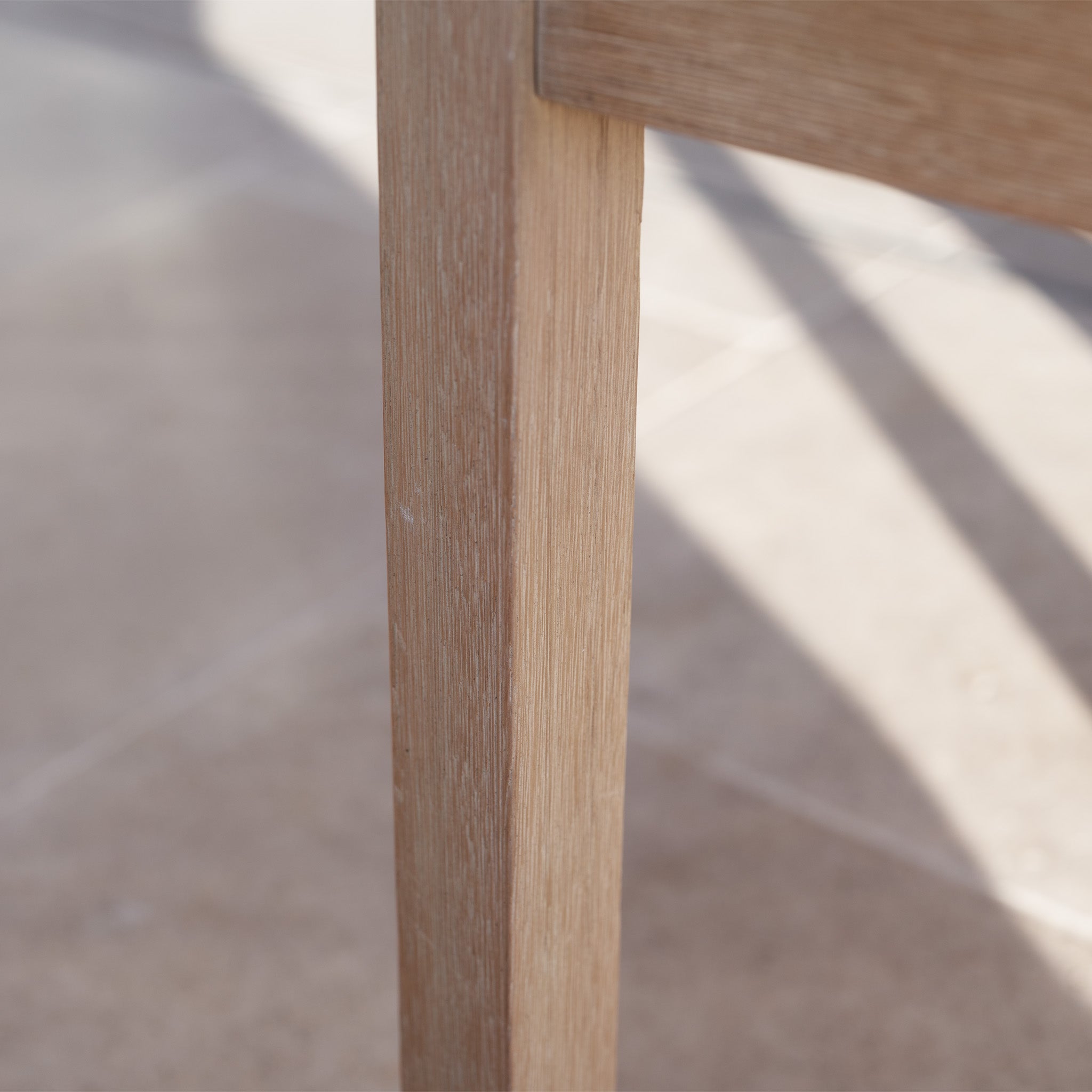 Close-up of a Quay 4 Seat Round Dining Set in Mocha leg casting a shadow on a tiled floor in natural light.