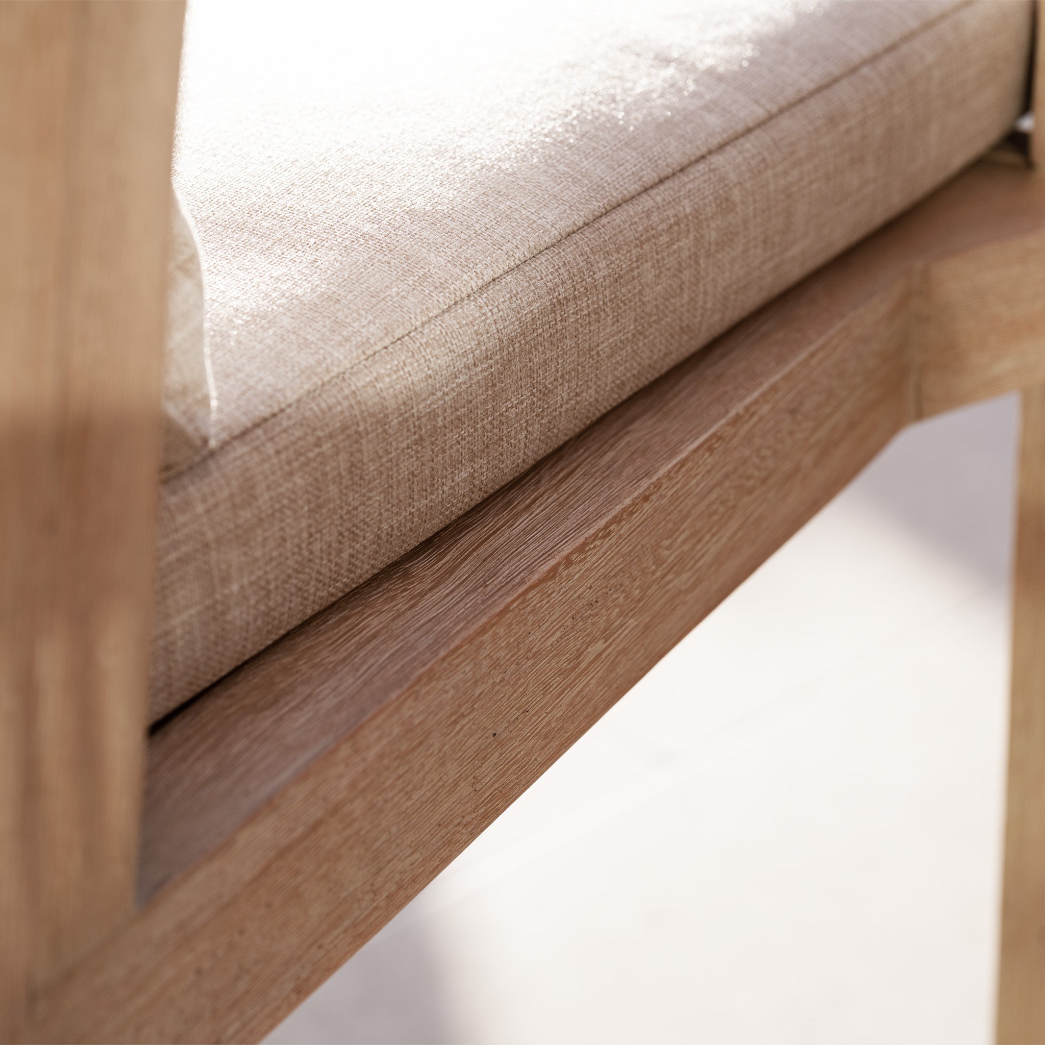 Close-up of the Quay Corner Sofa Dining Set in Mocha, featuring a beige cushioned seat and a wooden frame with a rope-weave backrest, illuminated by gentle sunlight.