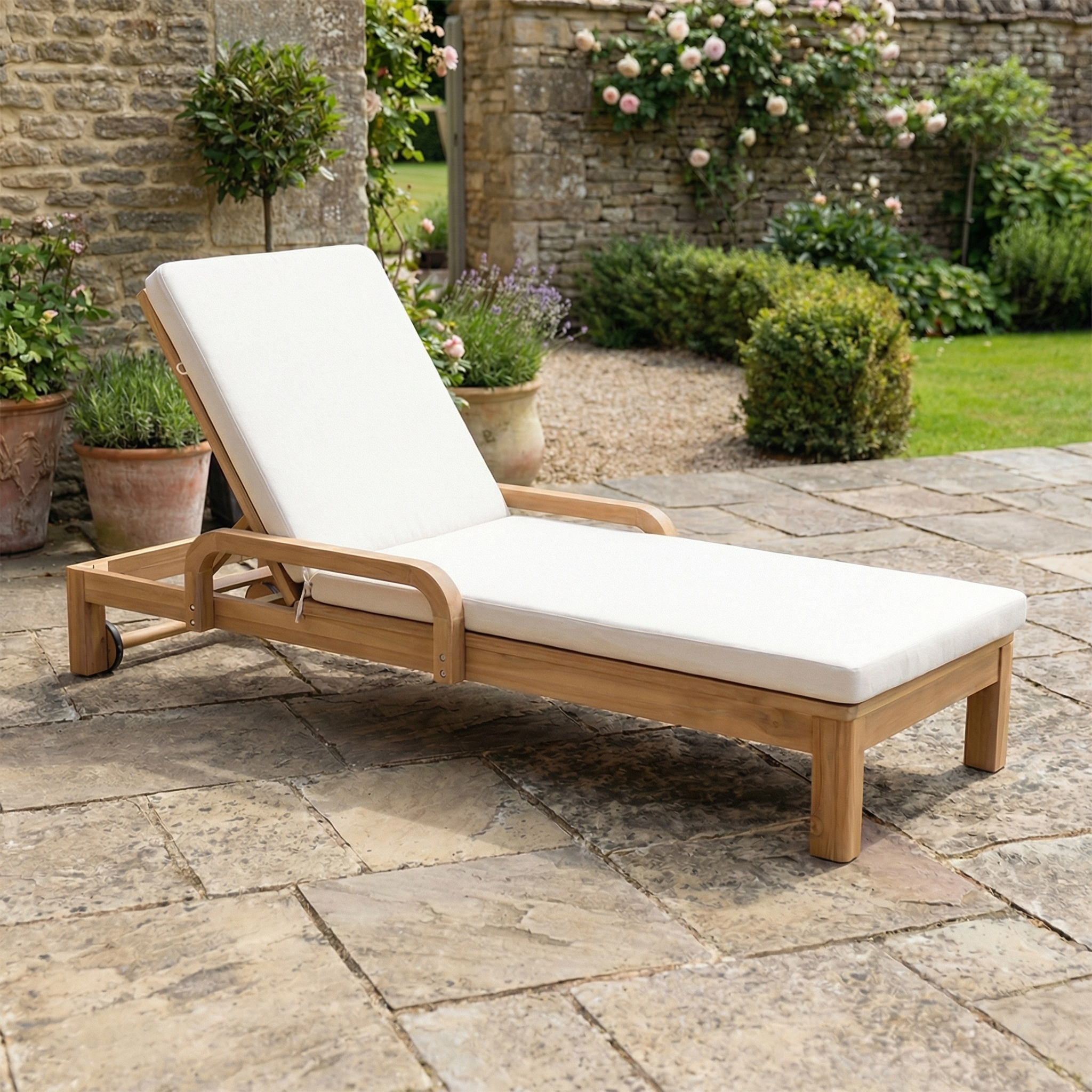 Quay Sun Lounger In Linen with white cushion on a stone patio, surrounded by garden greenery and potted plants—perfect stylish outdoor furniture for relaxing.